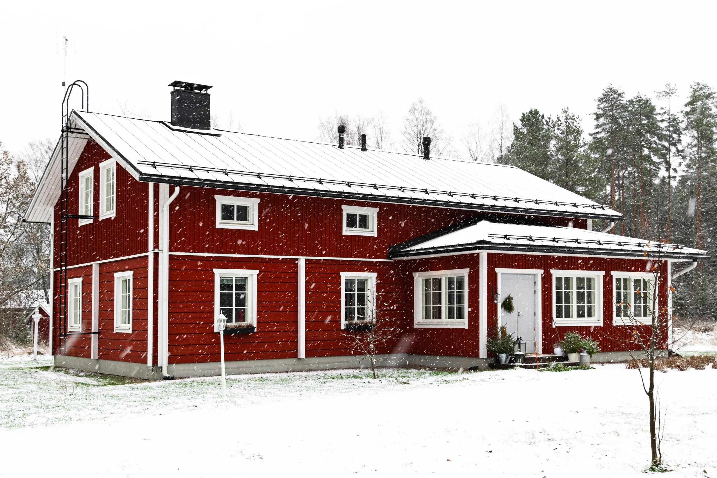 Punainen hirsitalo lumisateessa