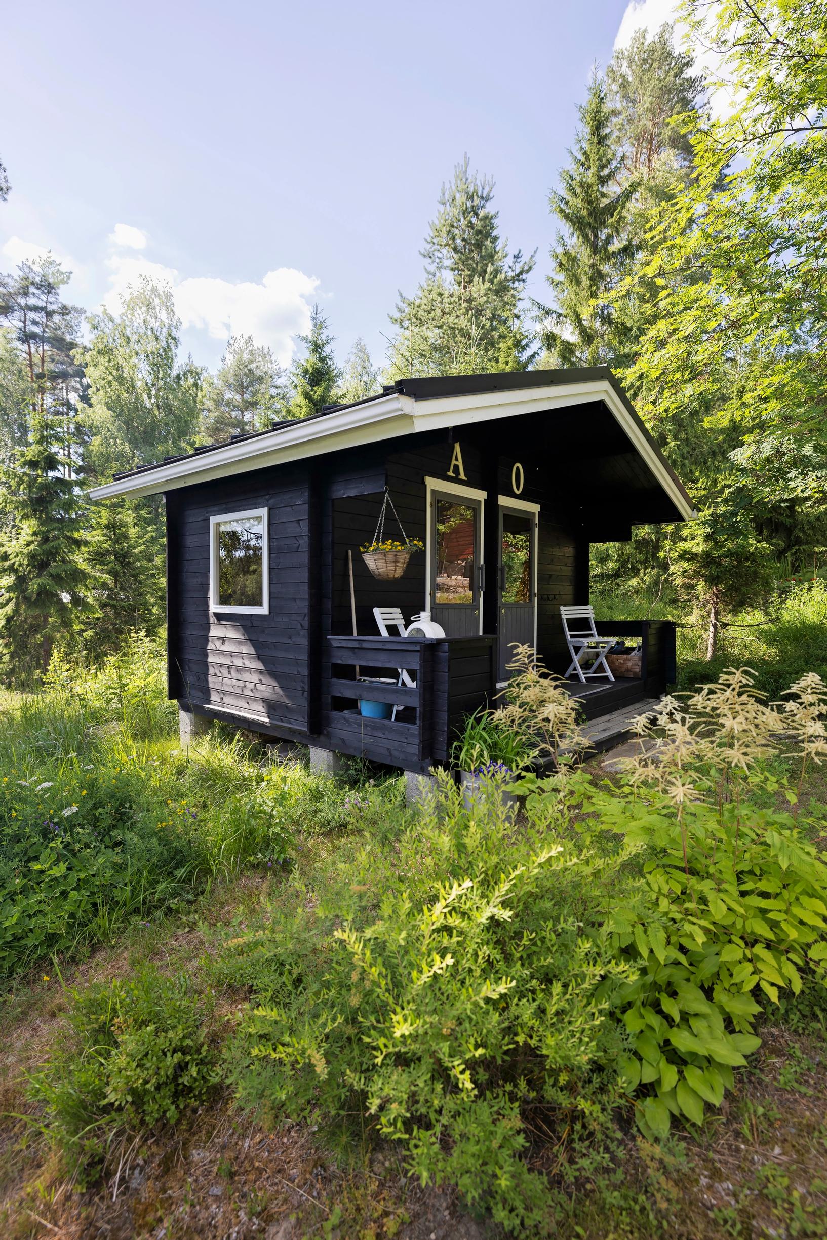 musta pieni aitta, metsää ja ympärillä vehreä puutarha