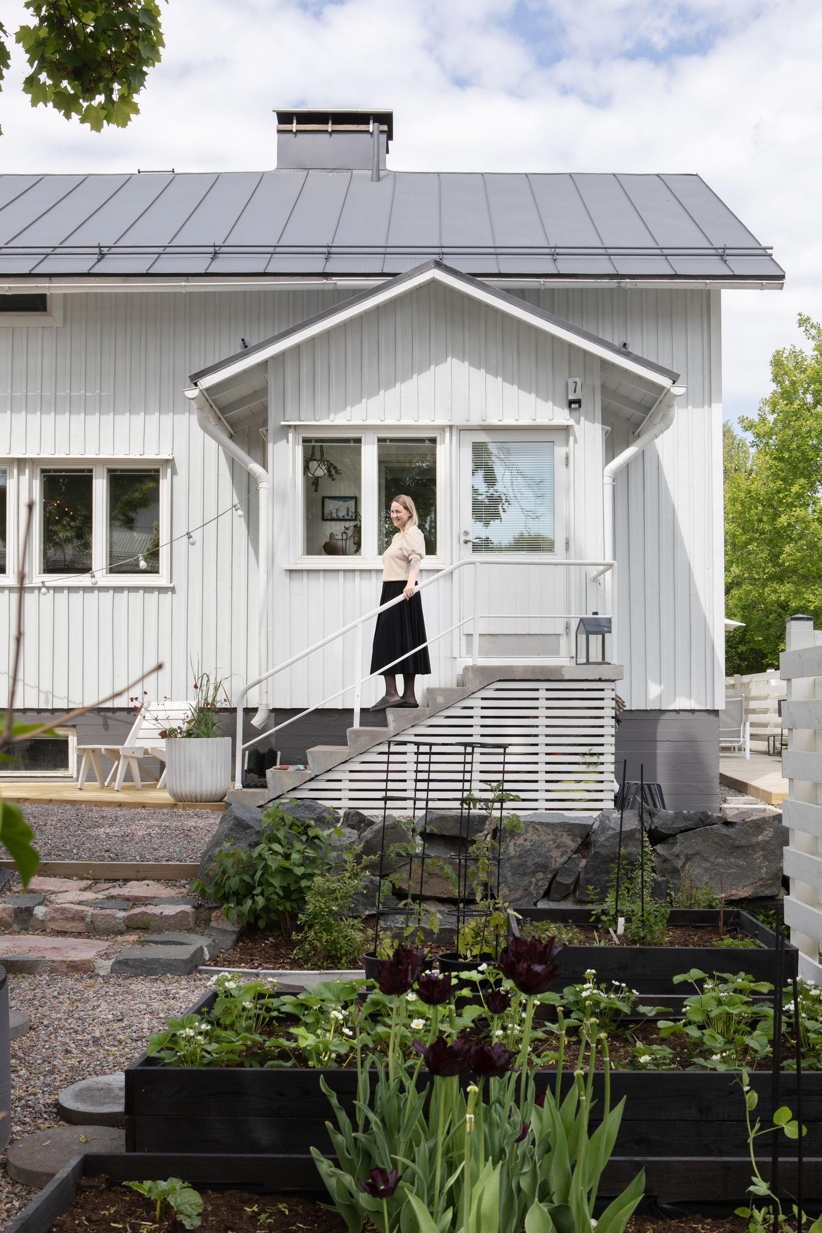 Outi omakotitalonsa kuistilla, etualalla viljelylaatikot.