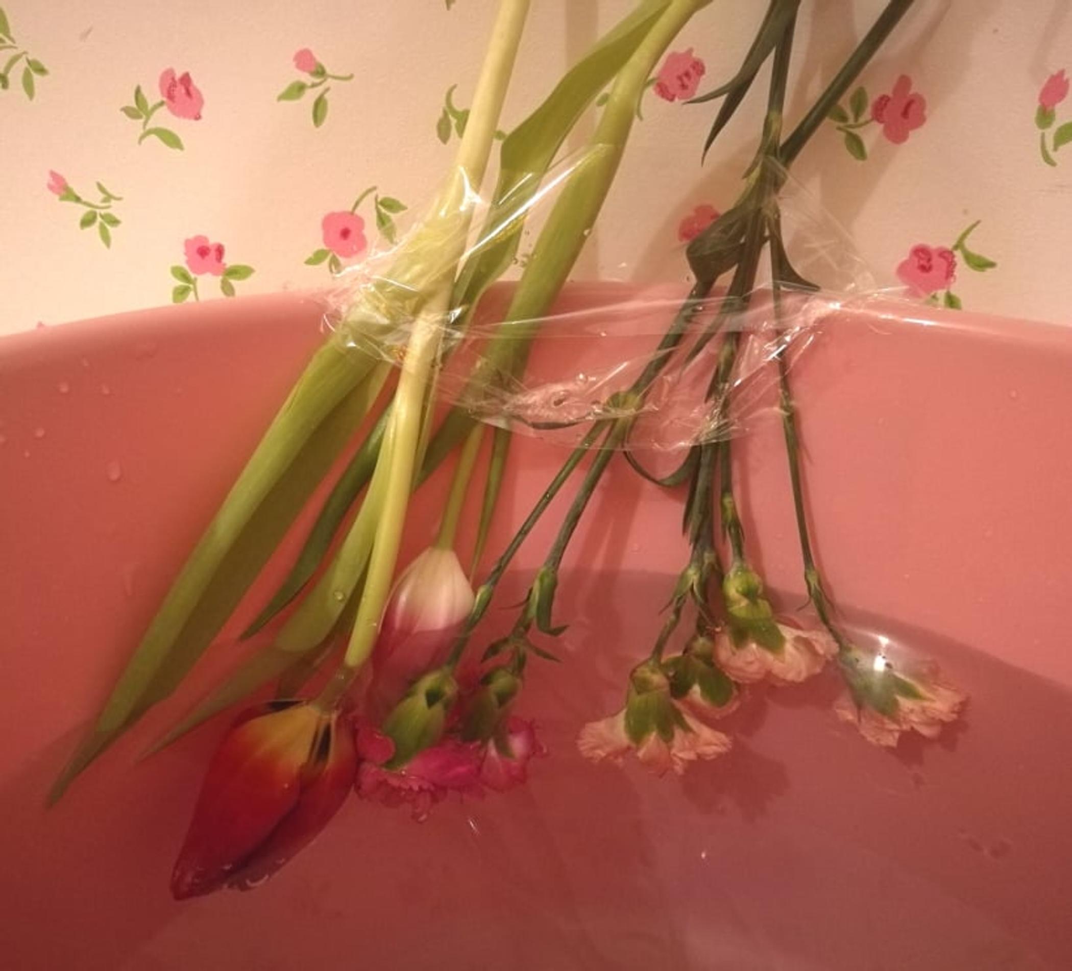 Kukkivan jäätornin tekovaihe: ämpärin reunaan teipattuja kukkia 