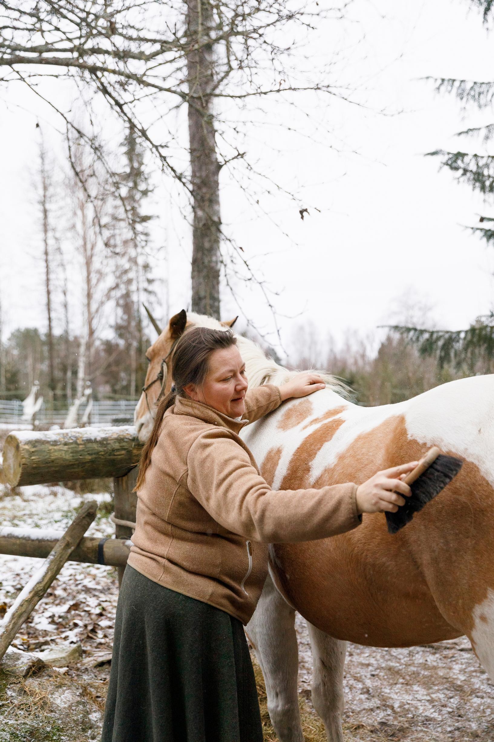 nainen harjaa ja silittää hevosta ulkoaitauksessa