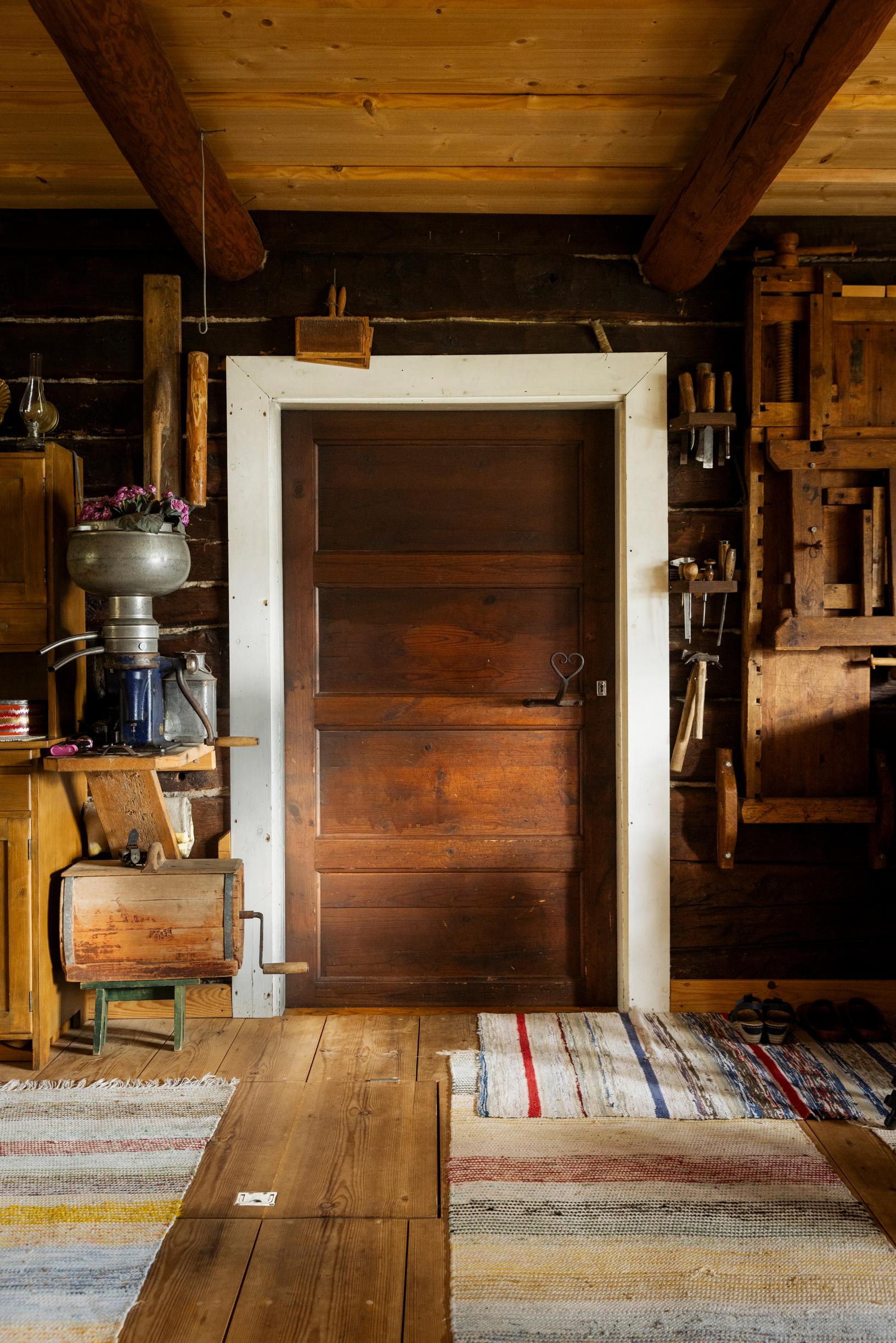 vanha ovi ja räsymattoja hirsitalossa, vanhoja esineitä seinällä