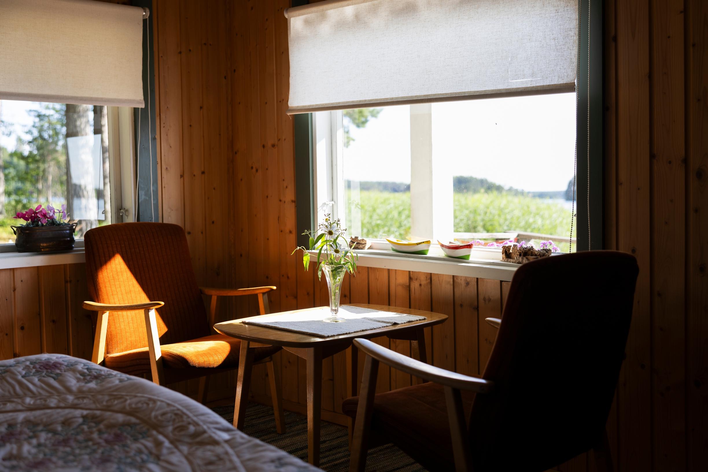 vanhat nojatuolit pienen pöydän ääressä, kaksi ikkunaa ja näkymä kaislikkoon ja järvelle