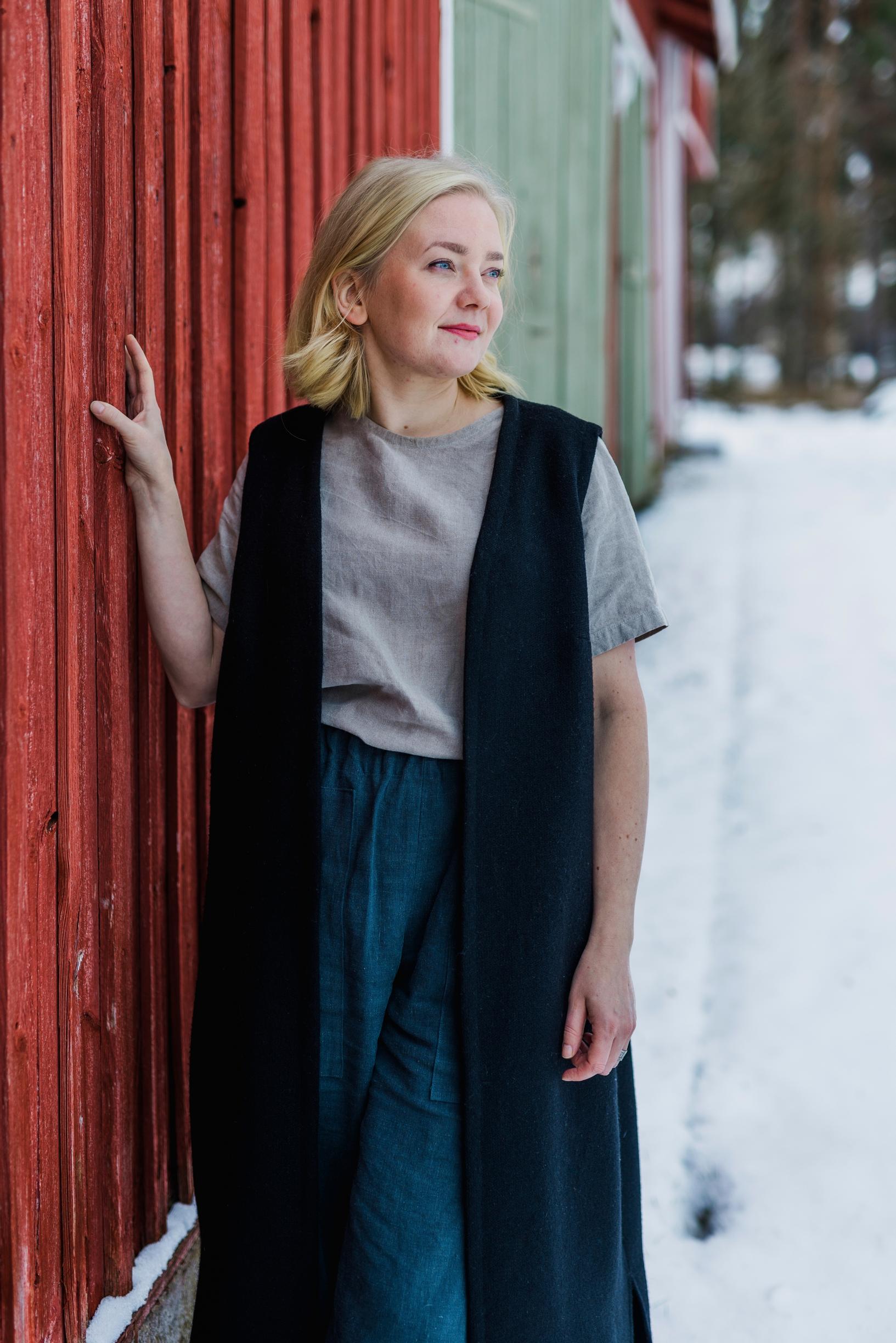 nainen seisoo puurakennuksen vieressä pihalla