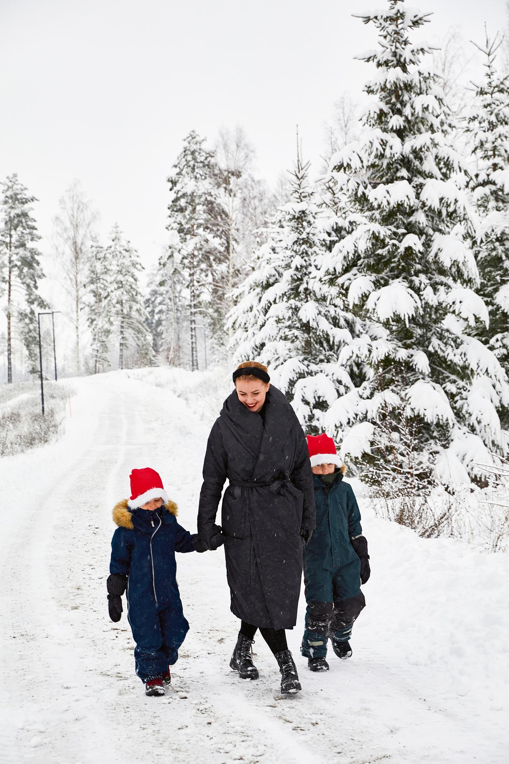 Julia ja tonttulakkiset pikkupojat kävelevät lumisella metsätiellä