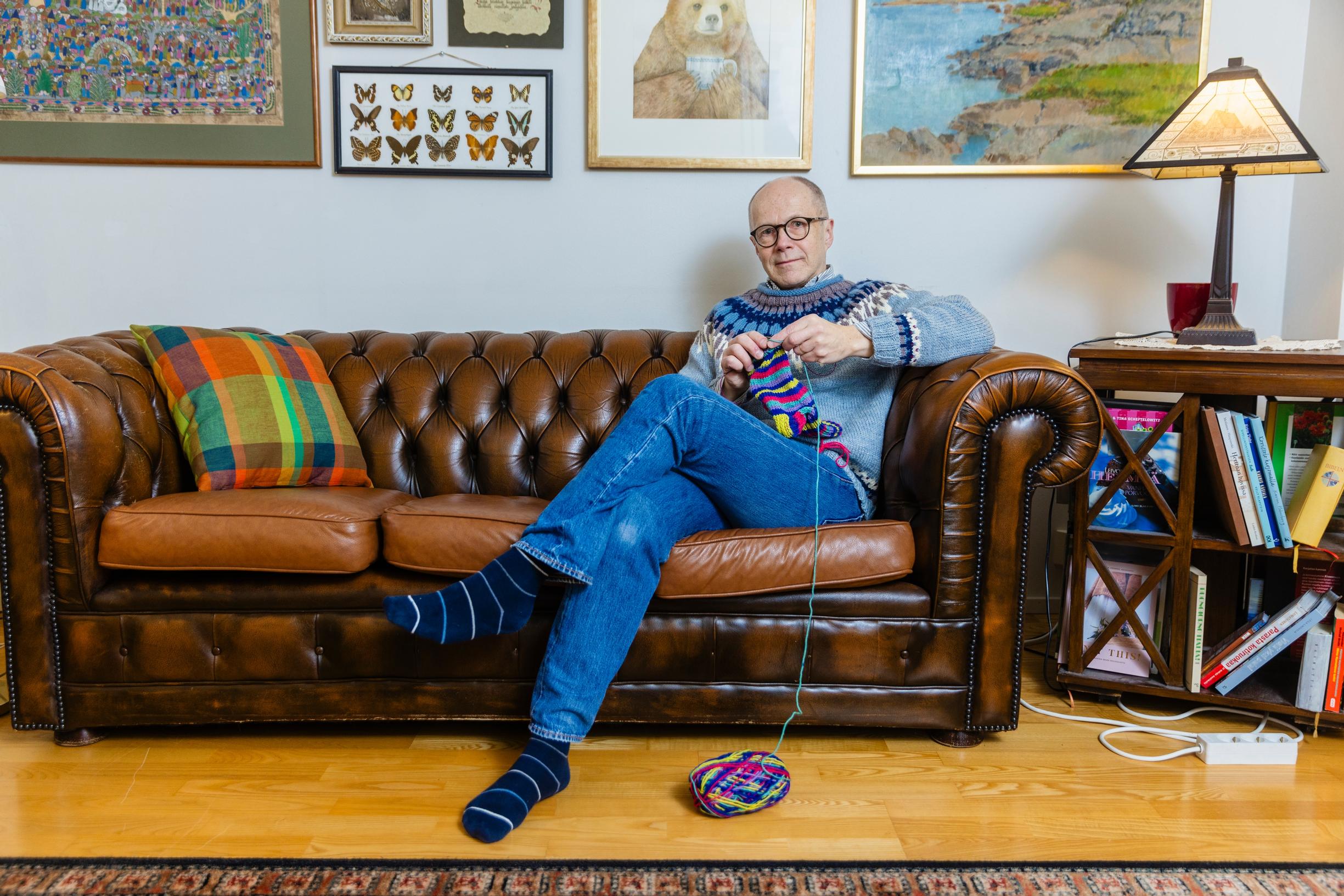 mies istuu nahkasohvalla neulomassa