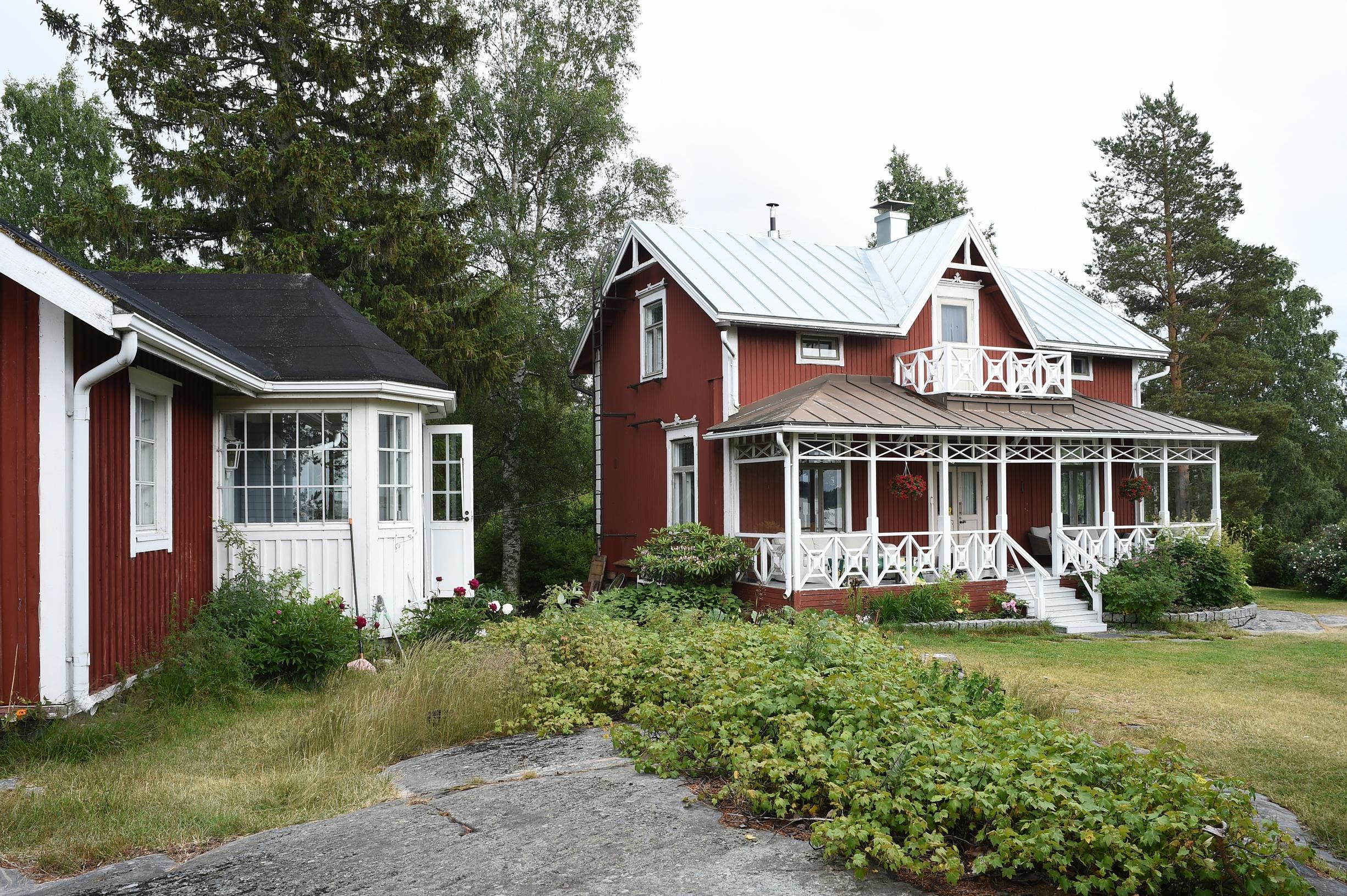 punainen vanha puuhuvila valkoisin ikkunanpielin ja samantapainen piharakennus metsänreunassa