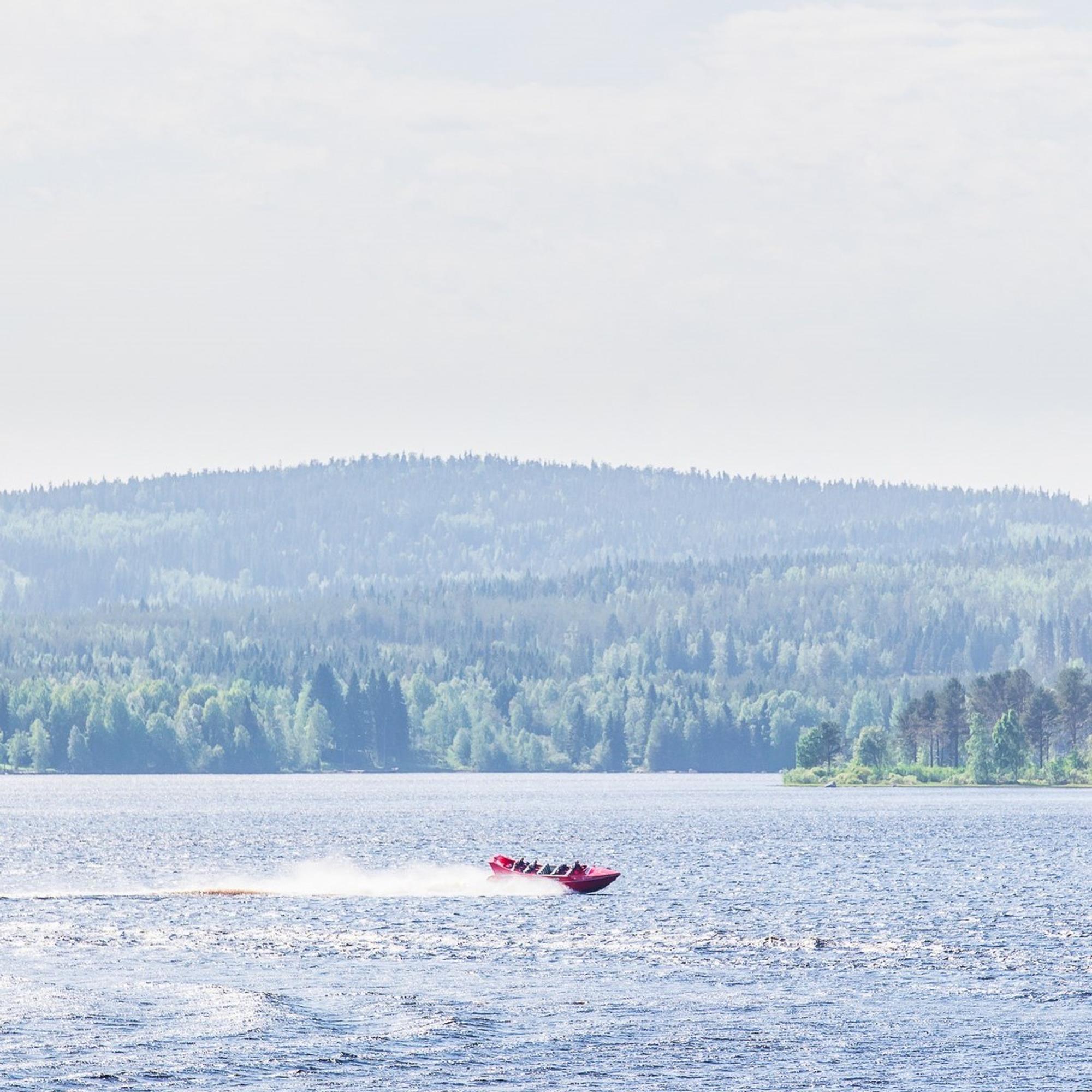 Kaukaa kuvattu kaunis järvimaisema, jossa kurvaa punainen speedboat-vene.
