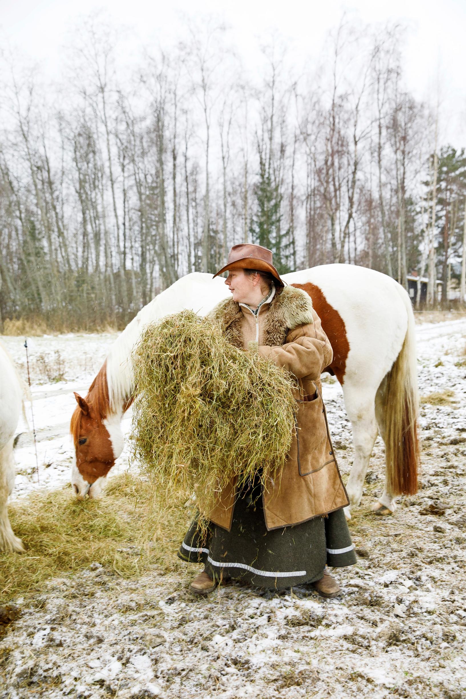 nainen antaa hevoselle heiniä