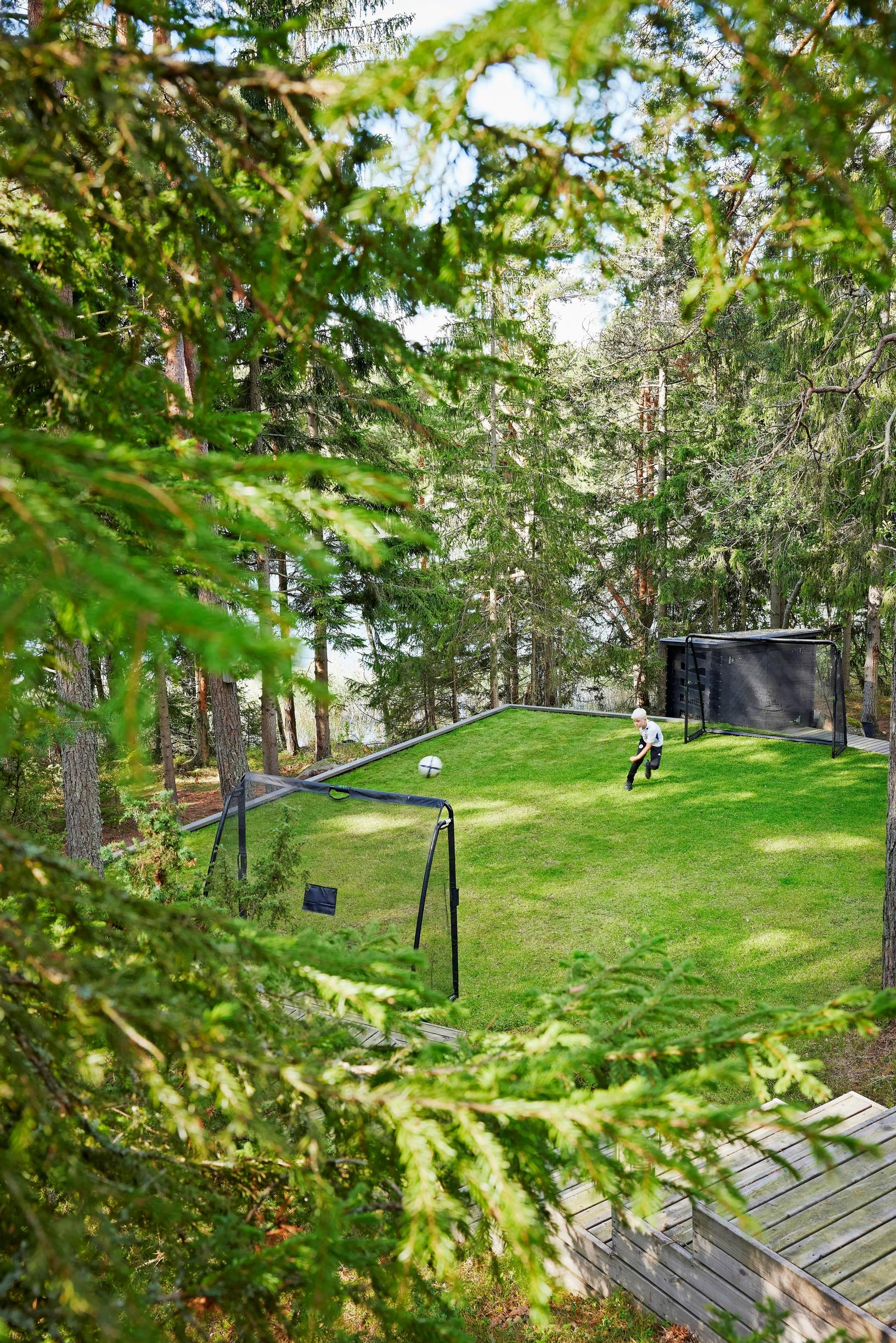 poika juoksee jalkapallokentällä metsän keskellä, taustalla järvi