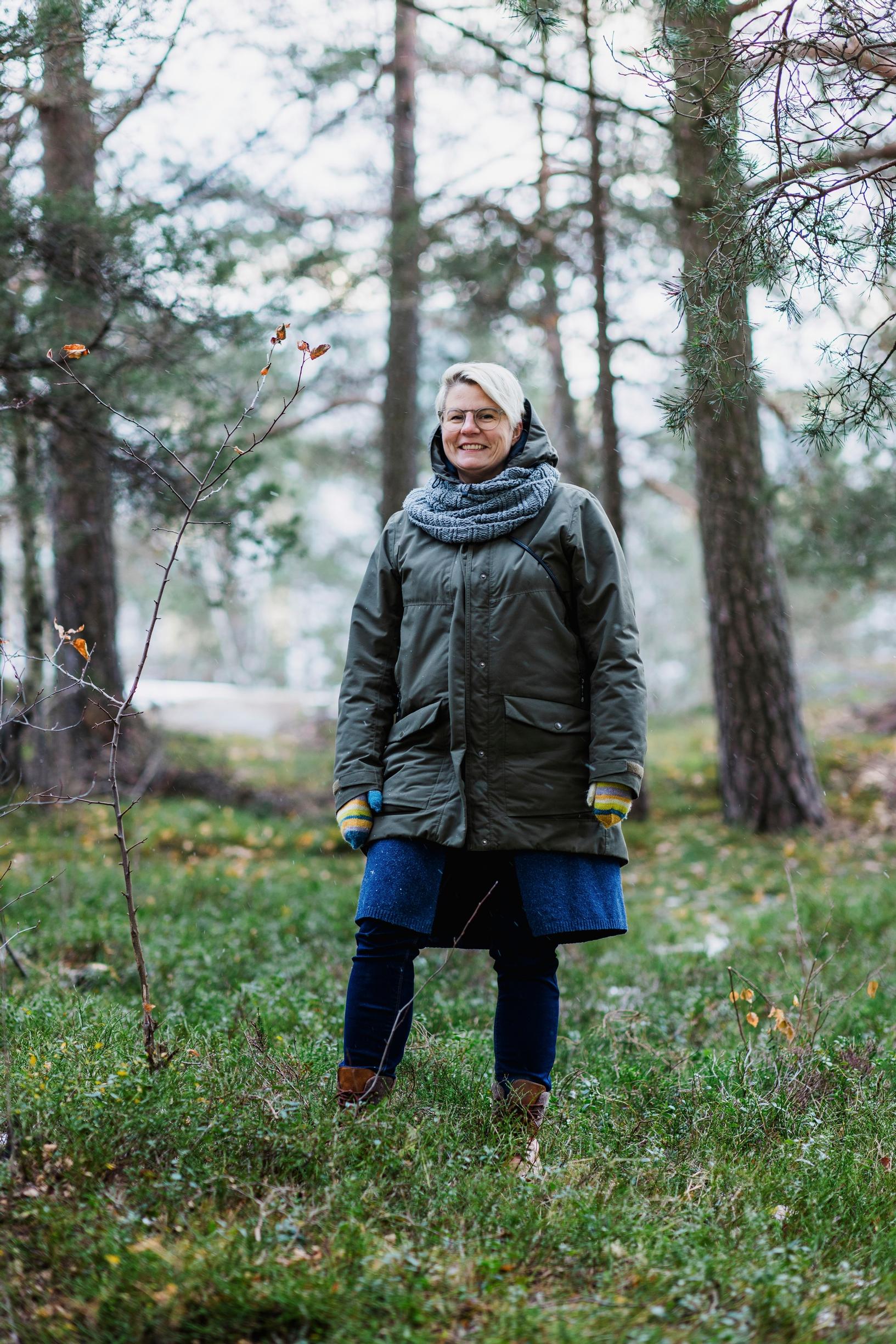 nainen seisoo mustikanvarpujen keskellä ja hymyilee