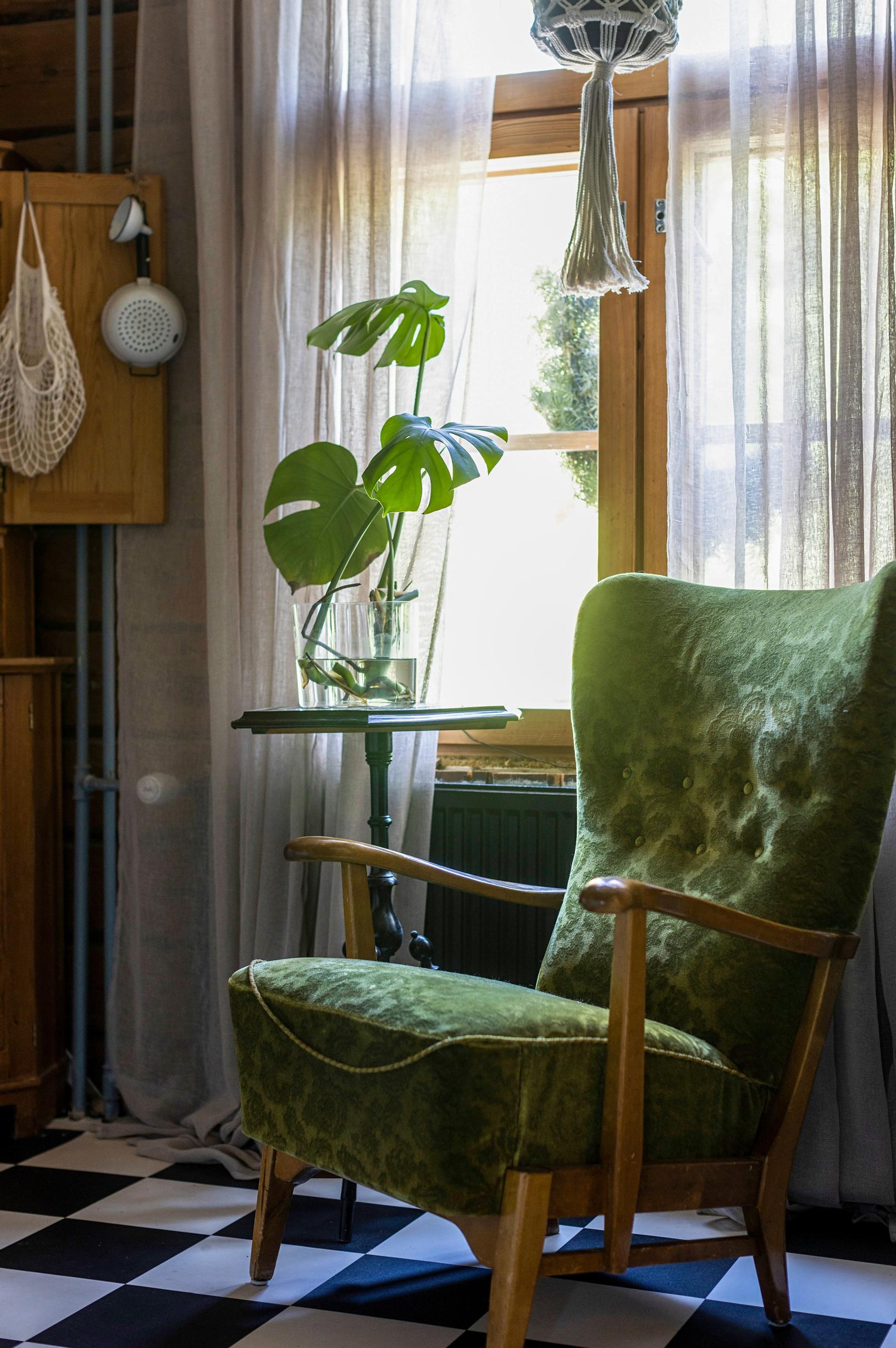 Vihreä samettinojatuoli ja peikonlehti pikkupöydällä