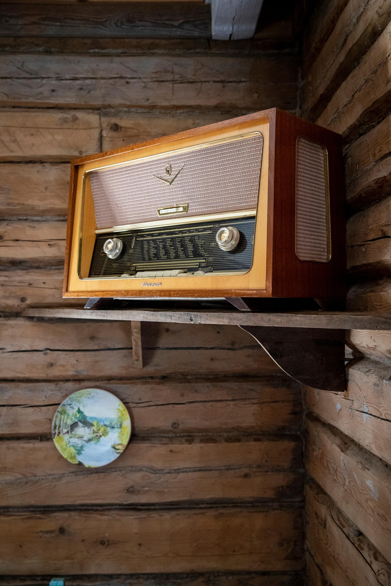 Vanha putkiradio hyllyllä ja hirsiseinää.