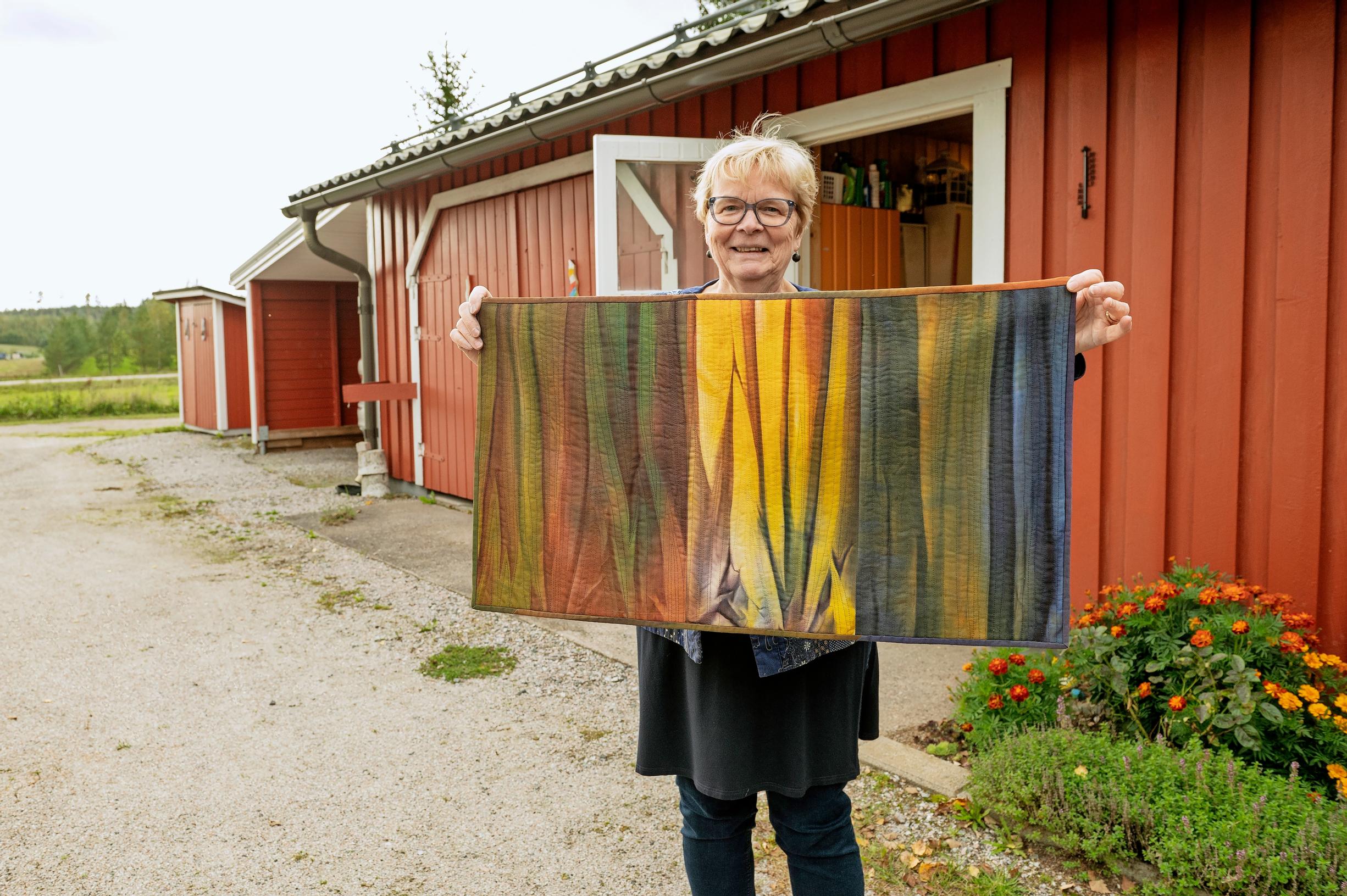 Pirjo Kekäläinen levittää pihalla värjäämään kankaita, taustalla punaisia rakennuksia