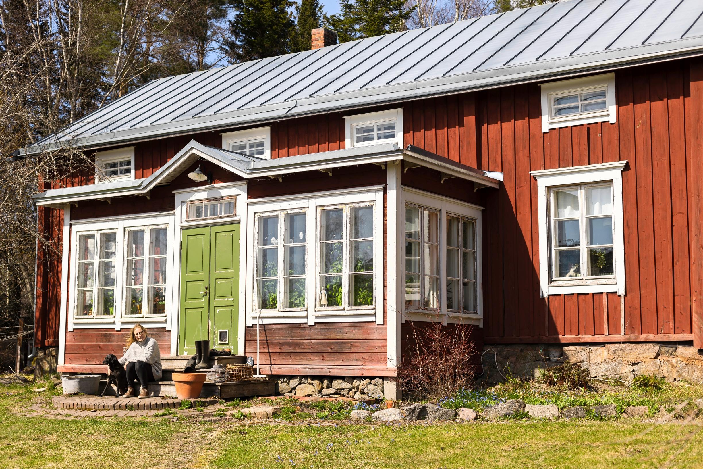 Nainen istuu punaisen puutalon portailla koiran kanssa