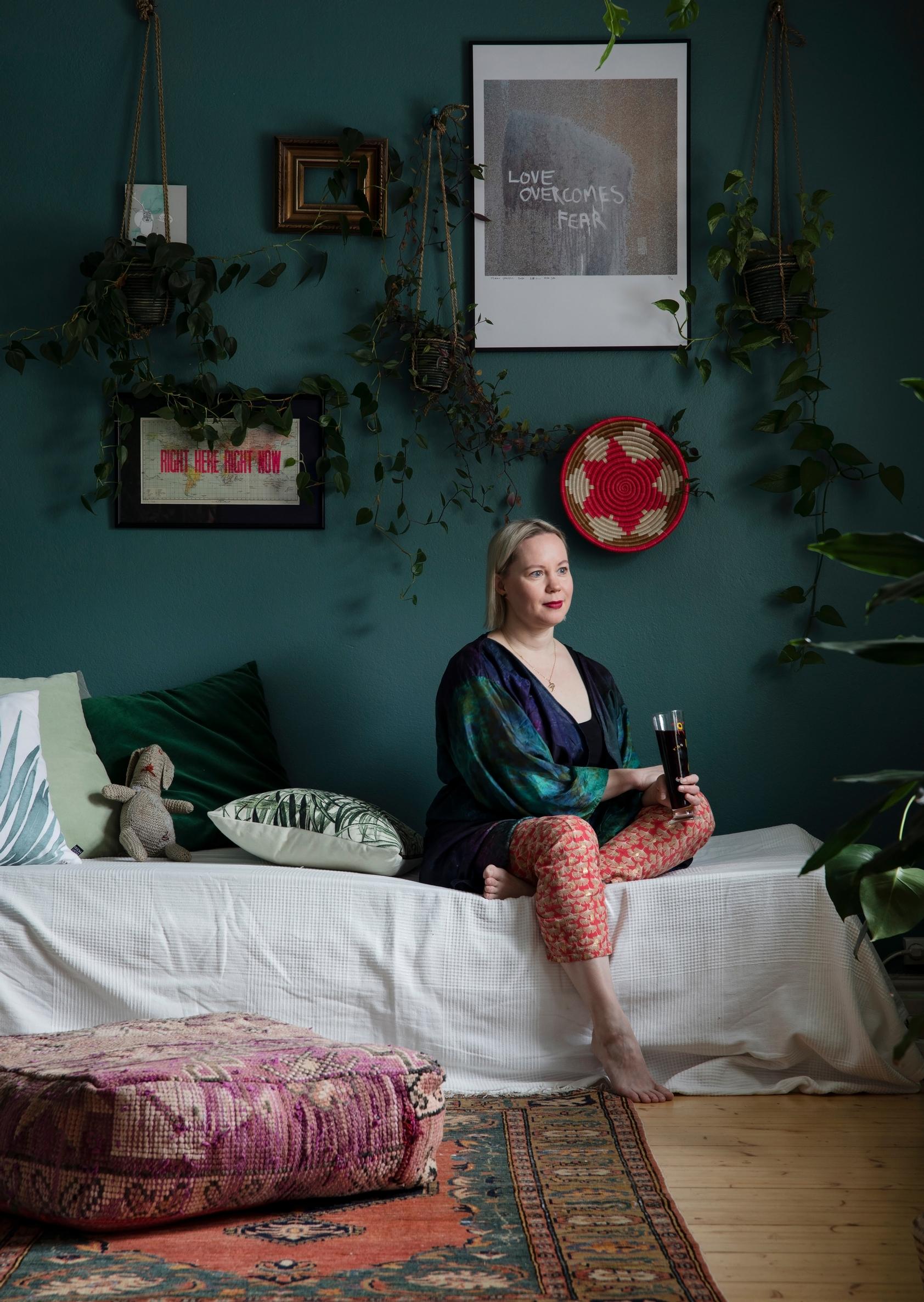 Erika istuu valkoisella sängyllä, taustallaan syvän vedenvihreä seinä