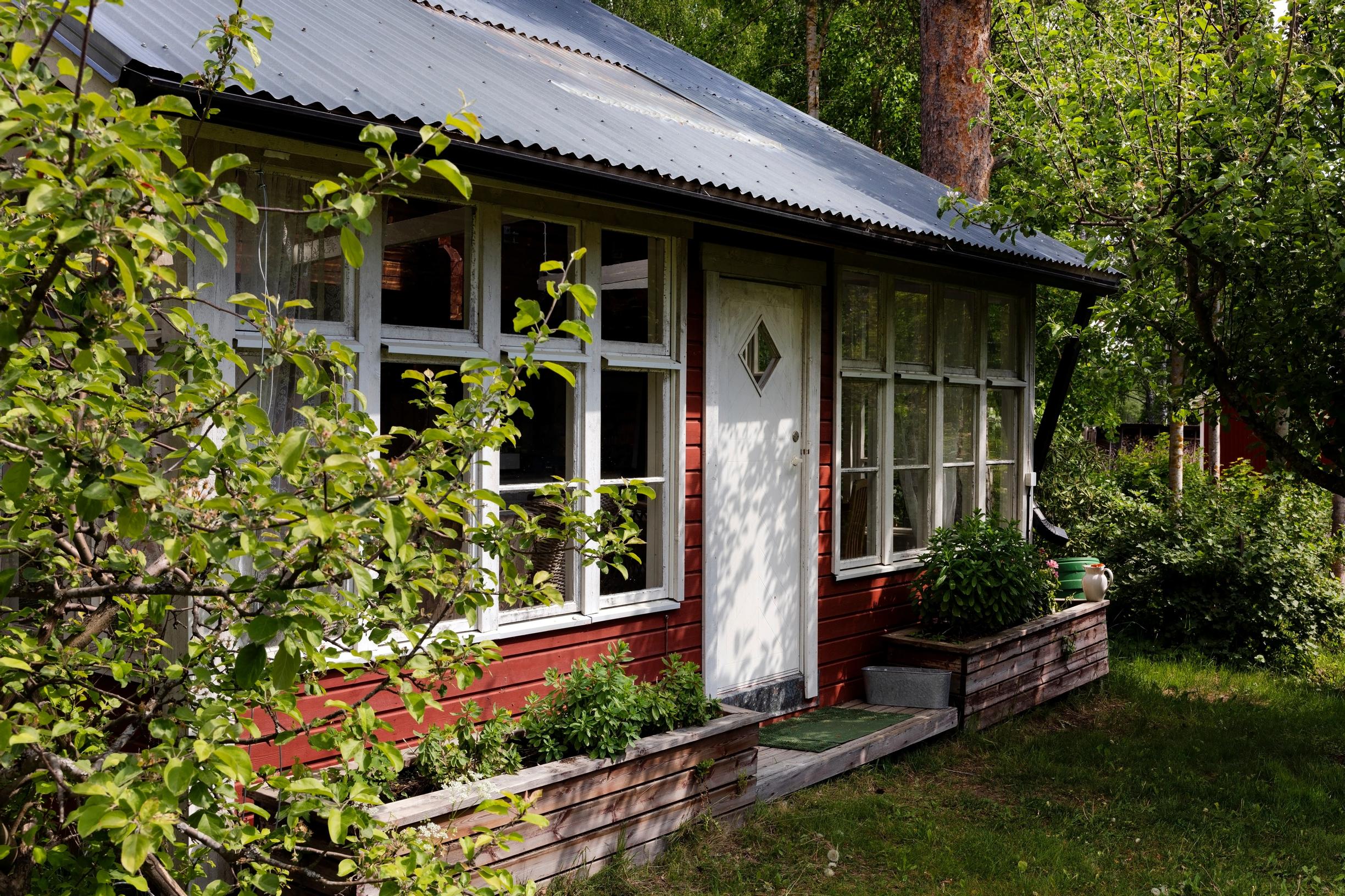 Aittarakennus vehreän puutarhan keskellä. Aitan ikkunat tehty kierrätysikkunoista.