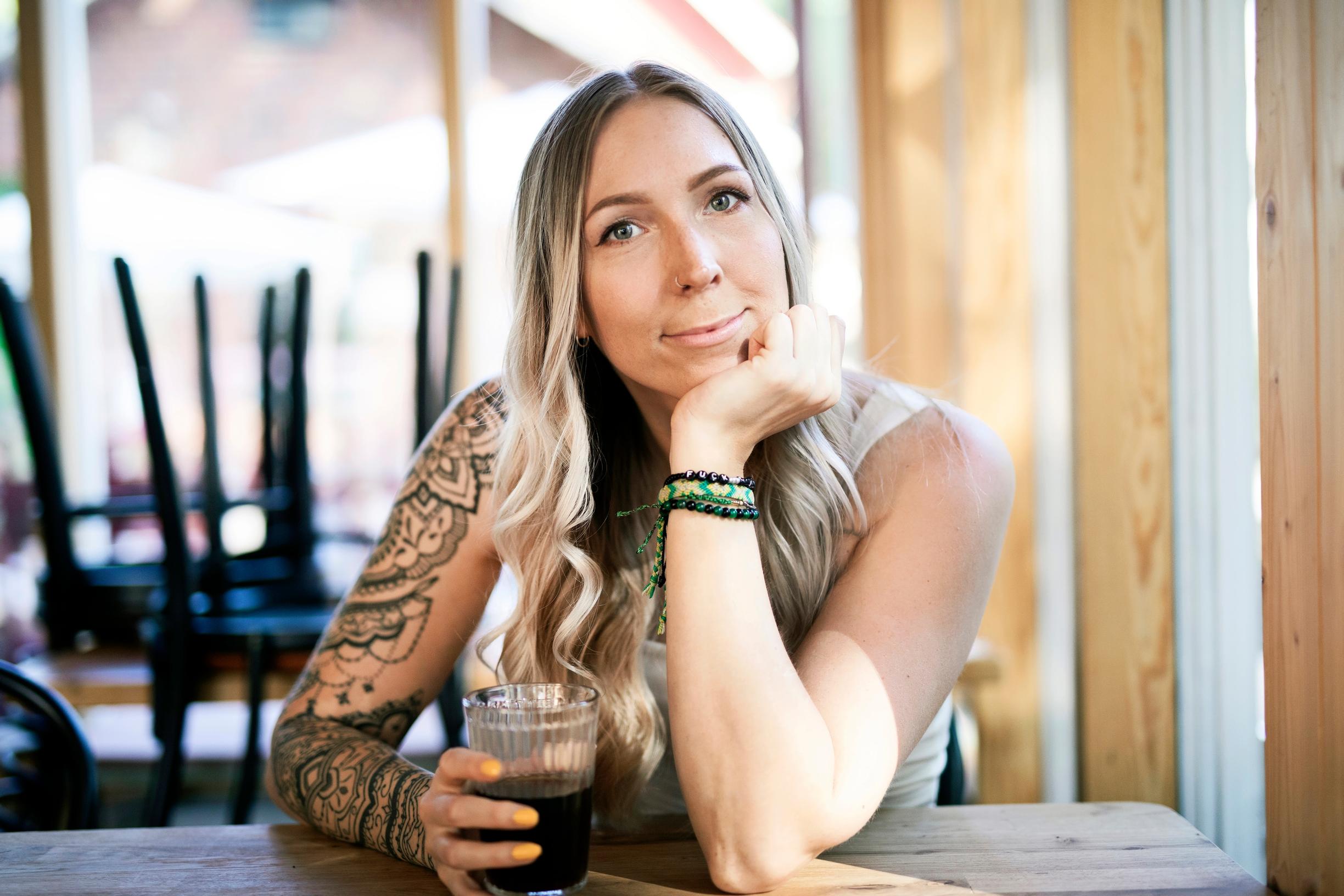 nainen istuu pöydän ääressä juomalasin kanssa
