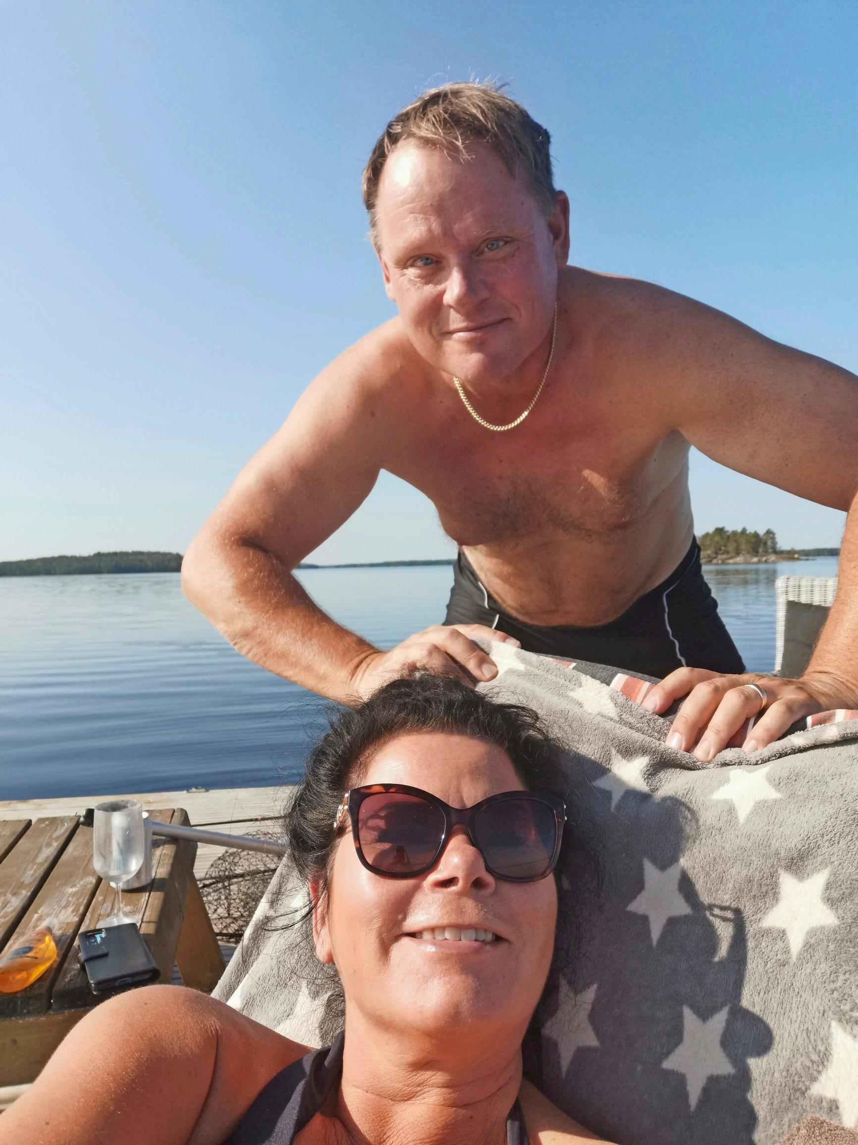 Markus Heiman ja vaimo Jaana saunalautalla aurinkoa ottamassa, taustalla tyyni järvenselkä