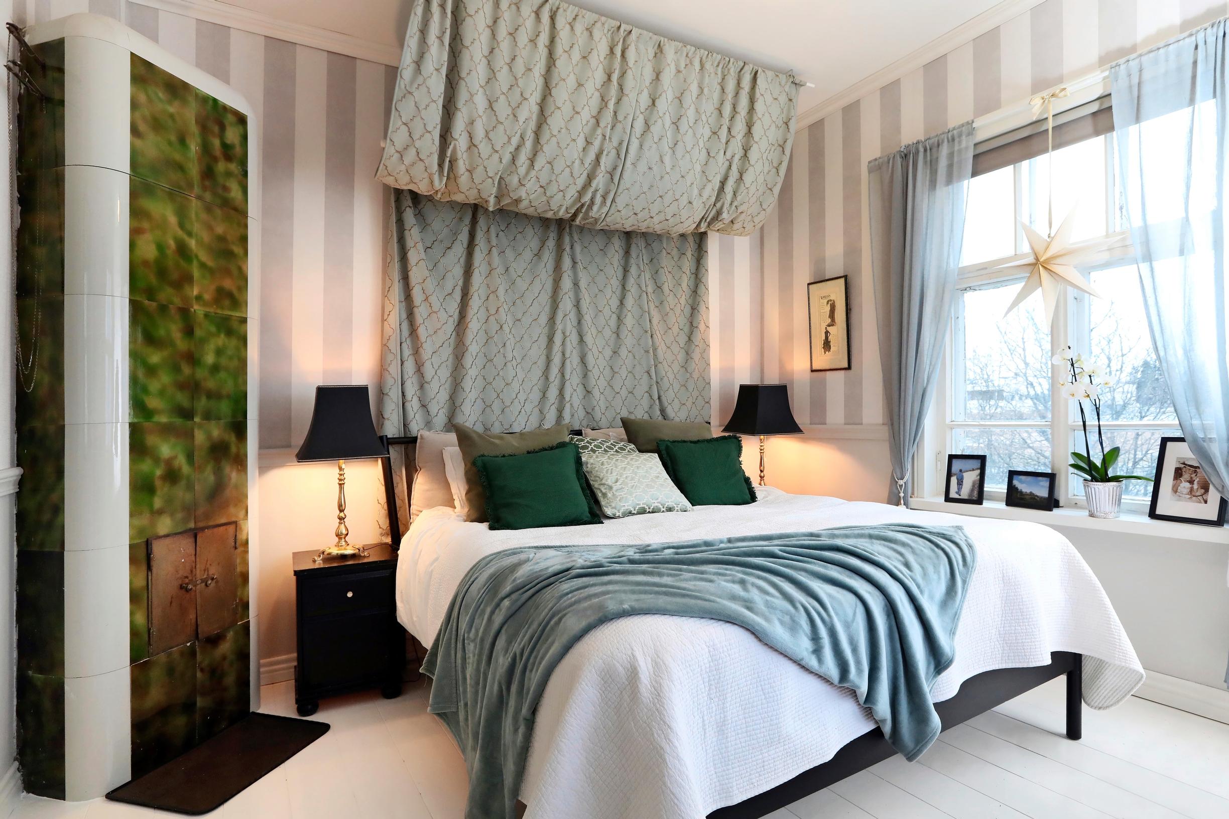 Vanhan ratsutilan makuuhuone, jossa on näyttävä sänkykatos ja vihreä kakluuni