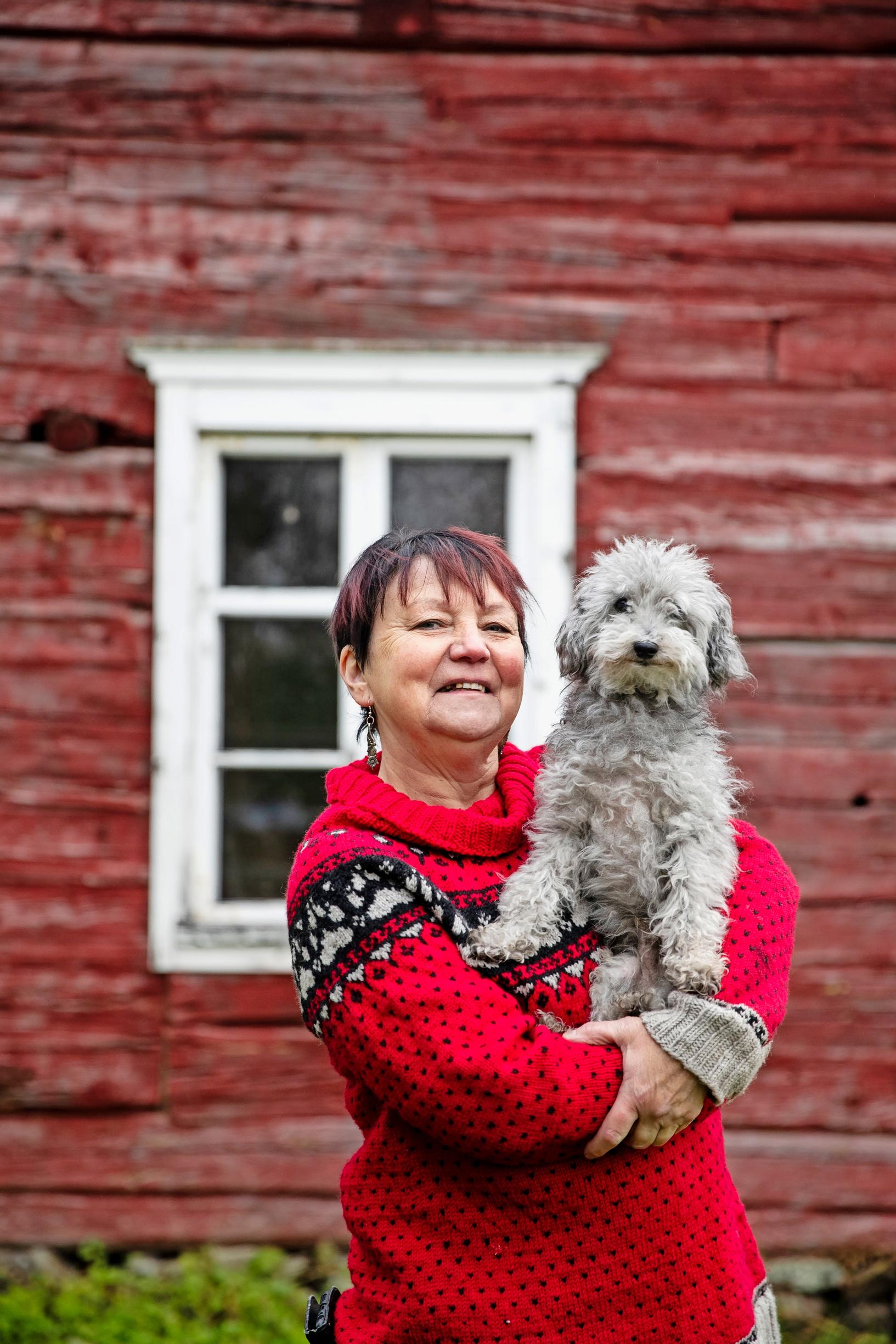 Päivi talon pihalla Oliver-koira sylissään.