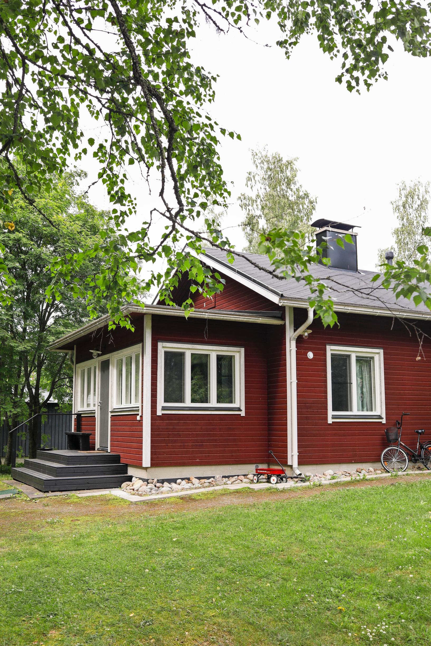 Punainen talo, valkoiset ikkunanpielet, puu ja nurmikkoa.