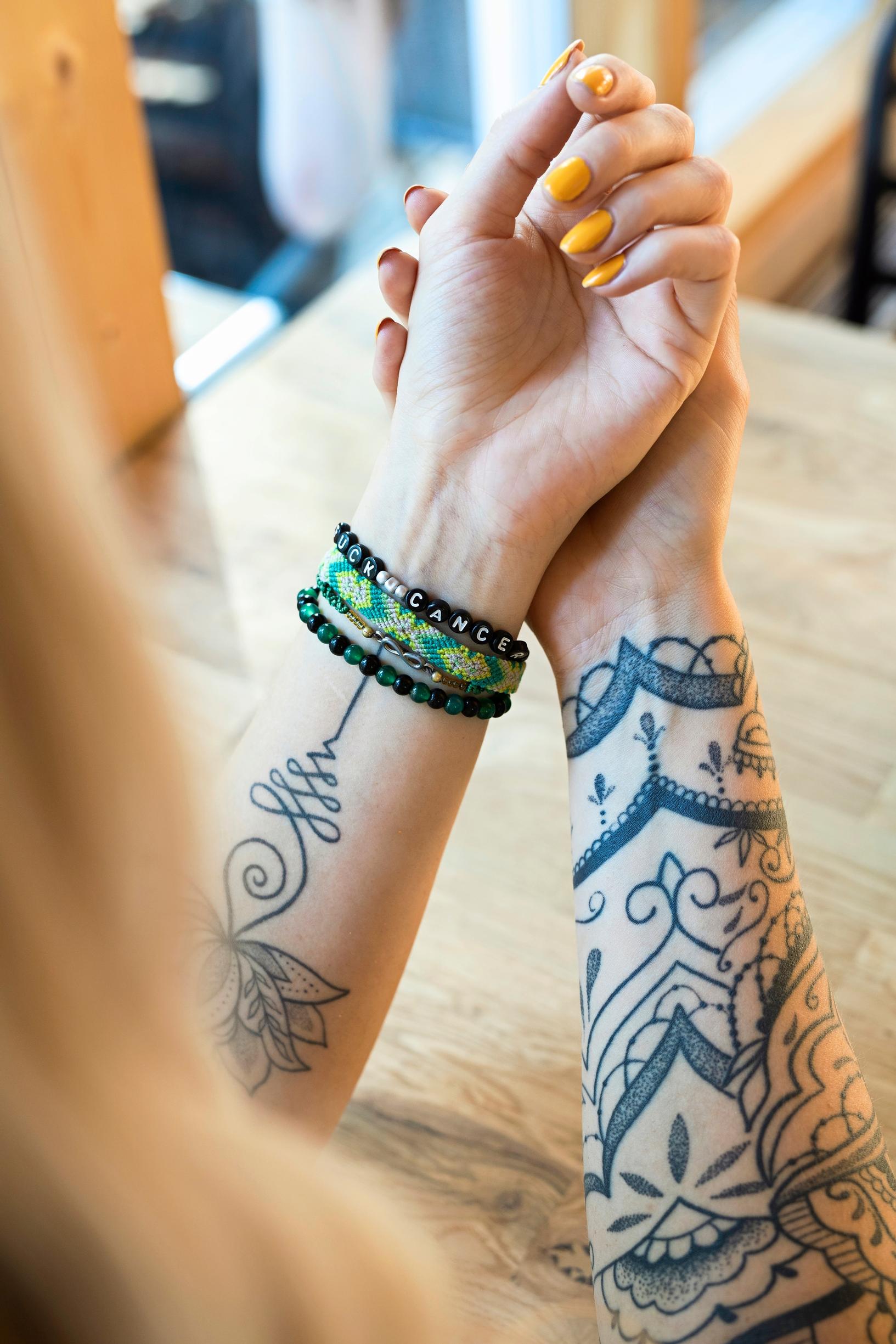 naisen tatuoidut kädet nojaavat pöytään