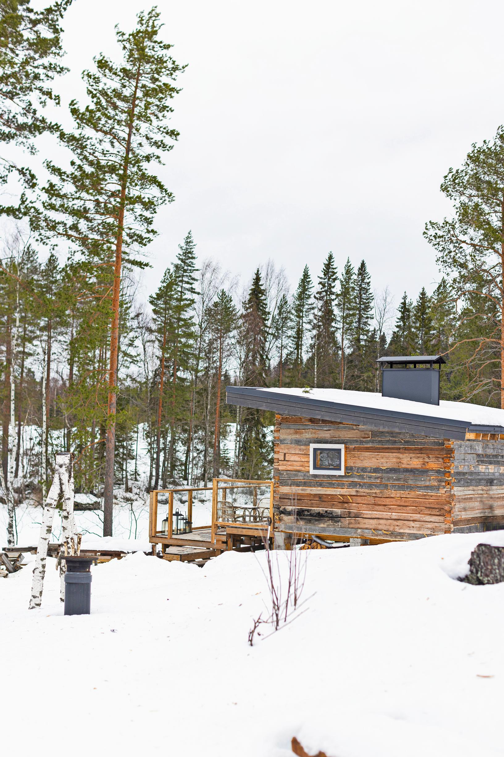 vanha hirsirakennus järven rannalla lumen keskellä, vastarannalla metsää