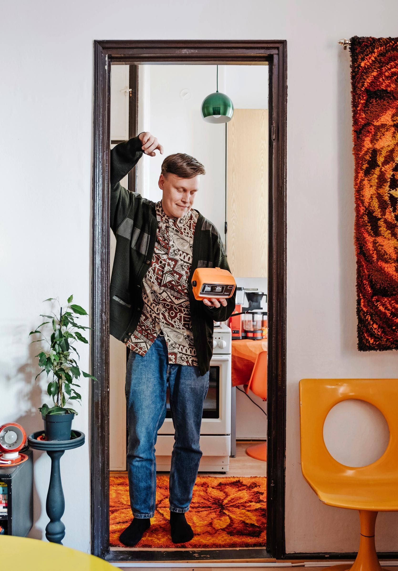 Kuva miehestä seisomassa retrohenkisesti sisustetun asunnon oviaukossa. 