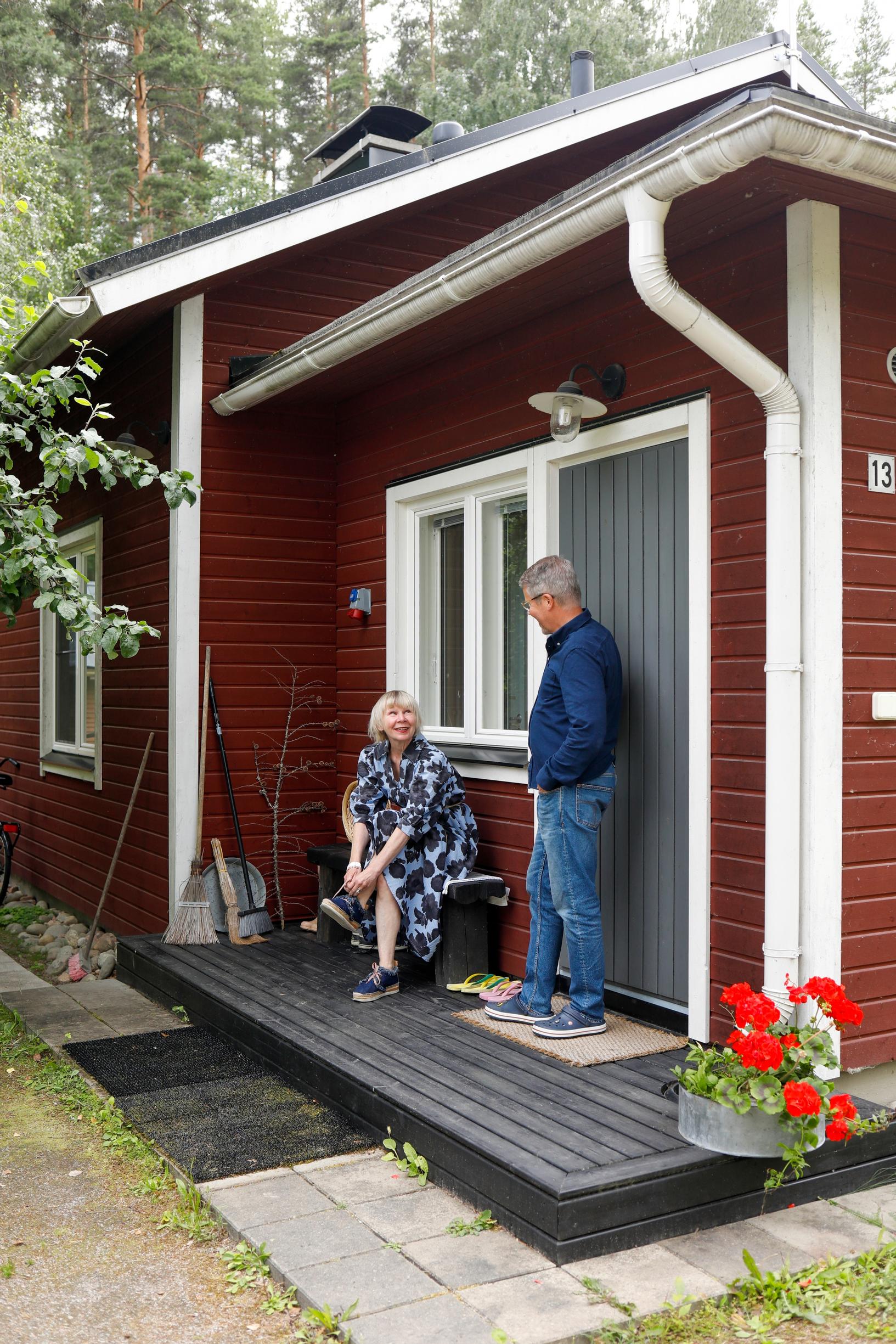 Nainen istuu ja mies seisoo mökin terassilla.