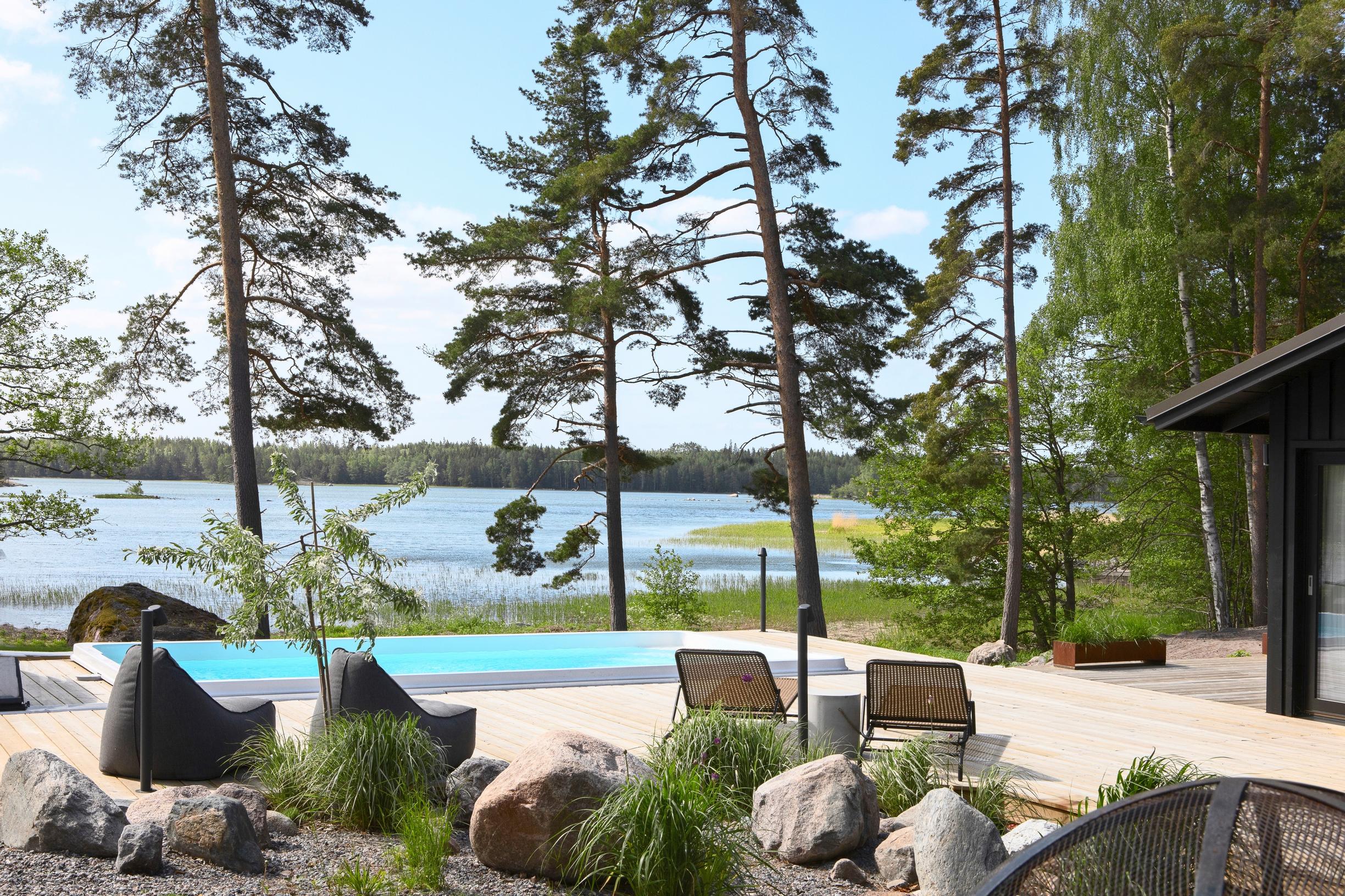 Porvoolaisen kesäasunnon terassilla uima-allas, näkymä merelle ja puita, etualalla puutarhakalusteita