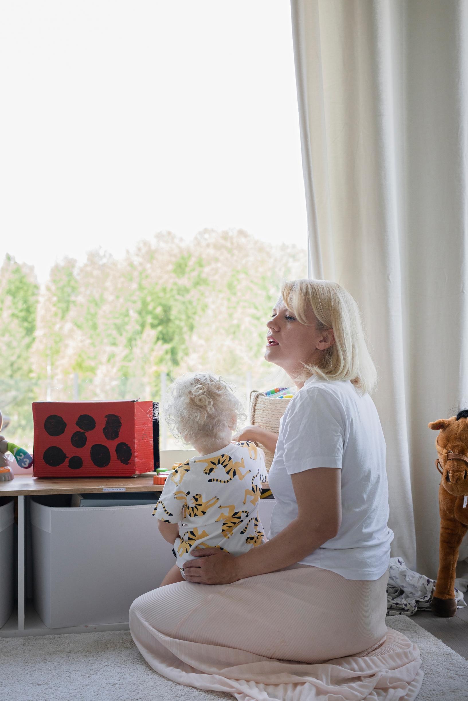 nainen istuu matolla lapsi sylissään