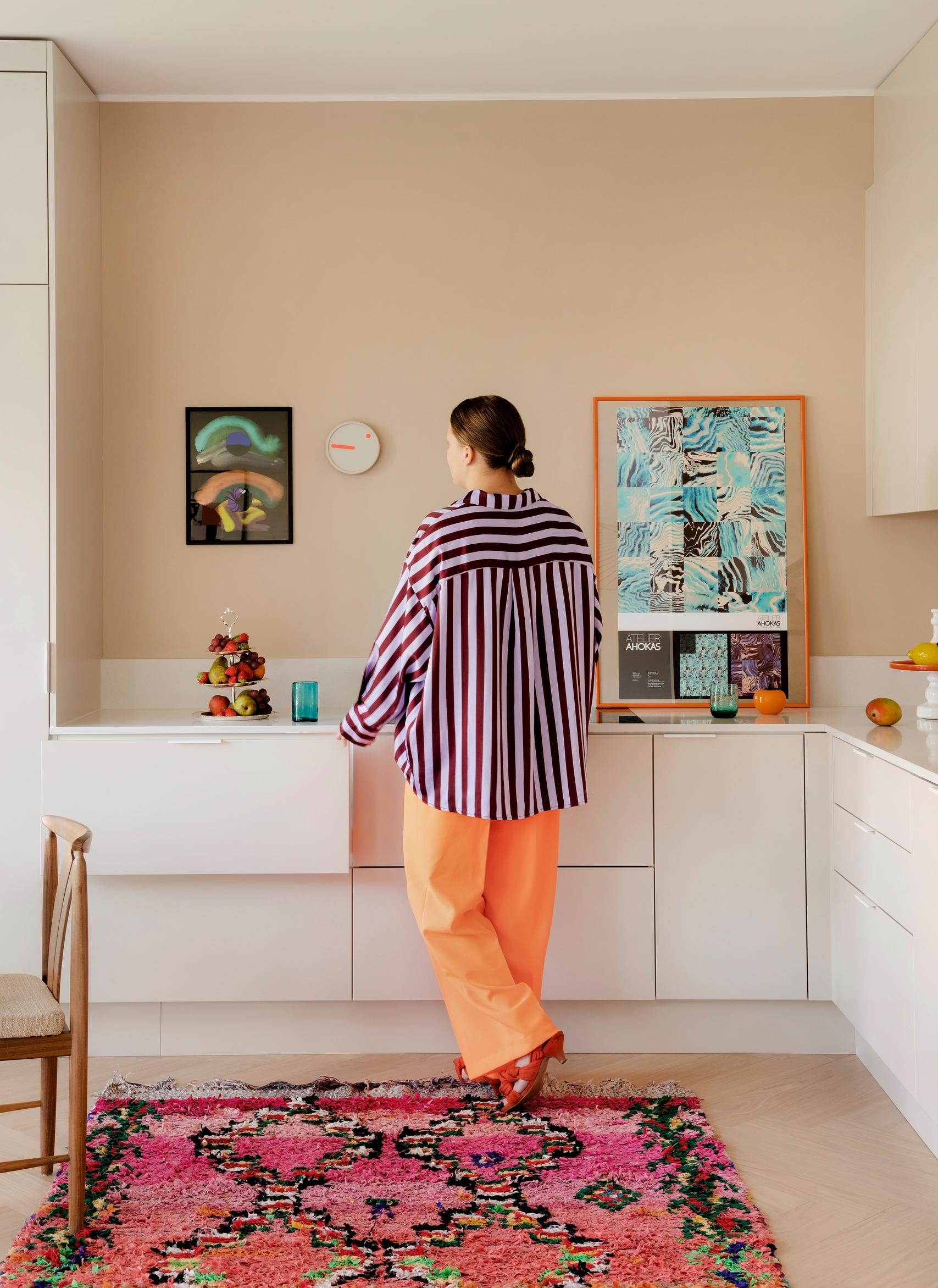 Valkoinen keittiö, jossa on beige seinä ja lattialla pinkki marokkolaismatto