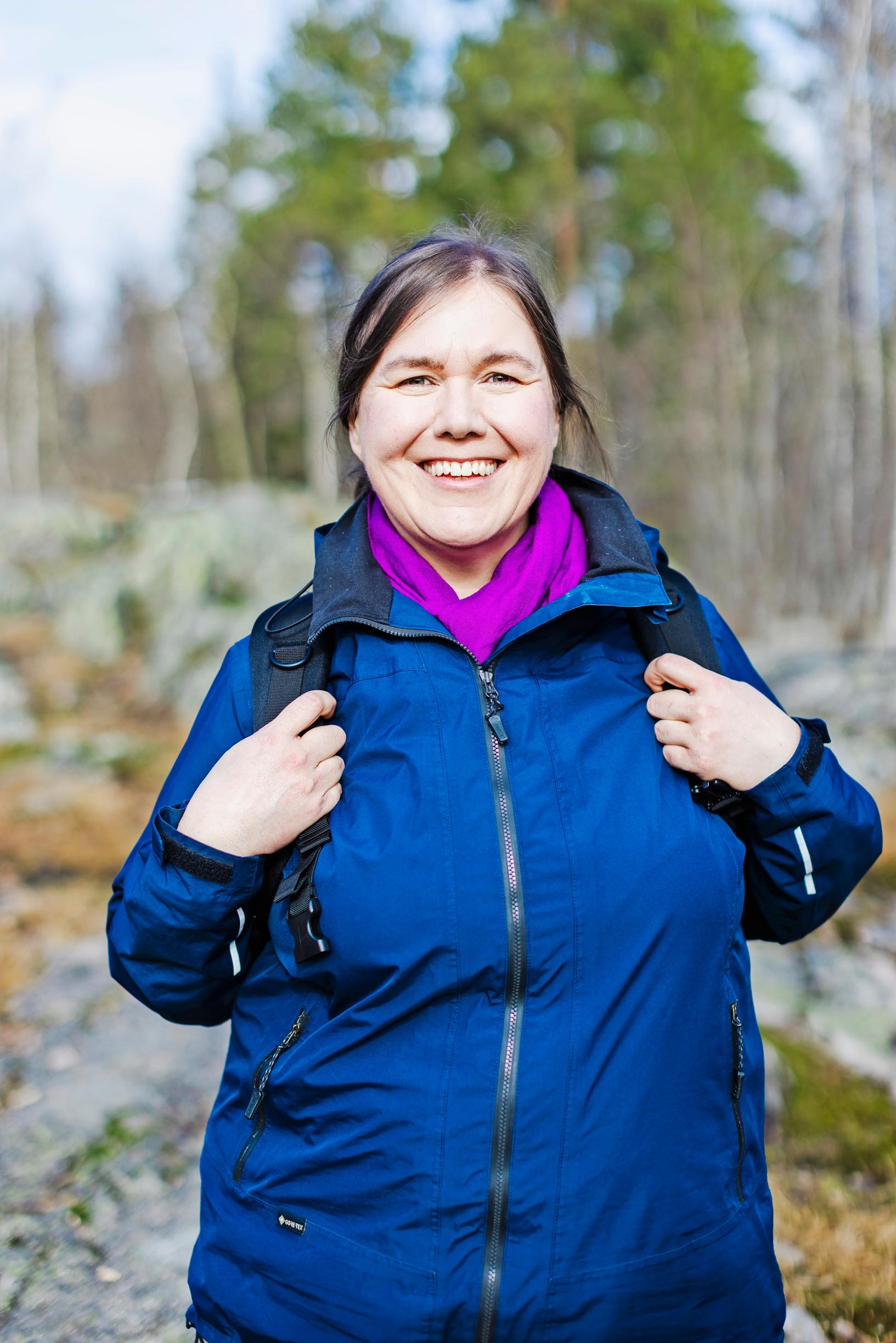 nainen pitää kiinni repun hihnoista ja hymyilee