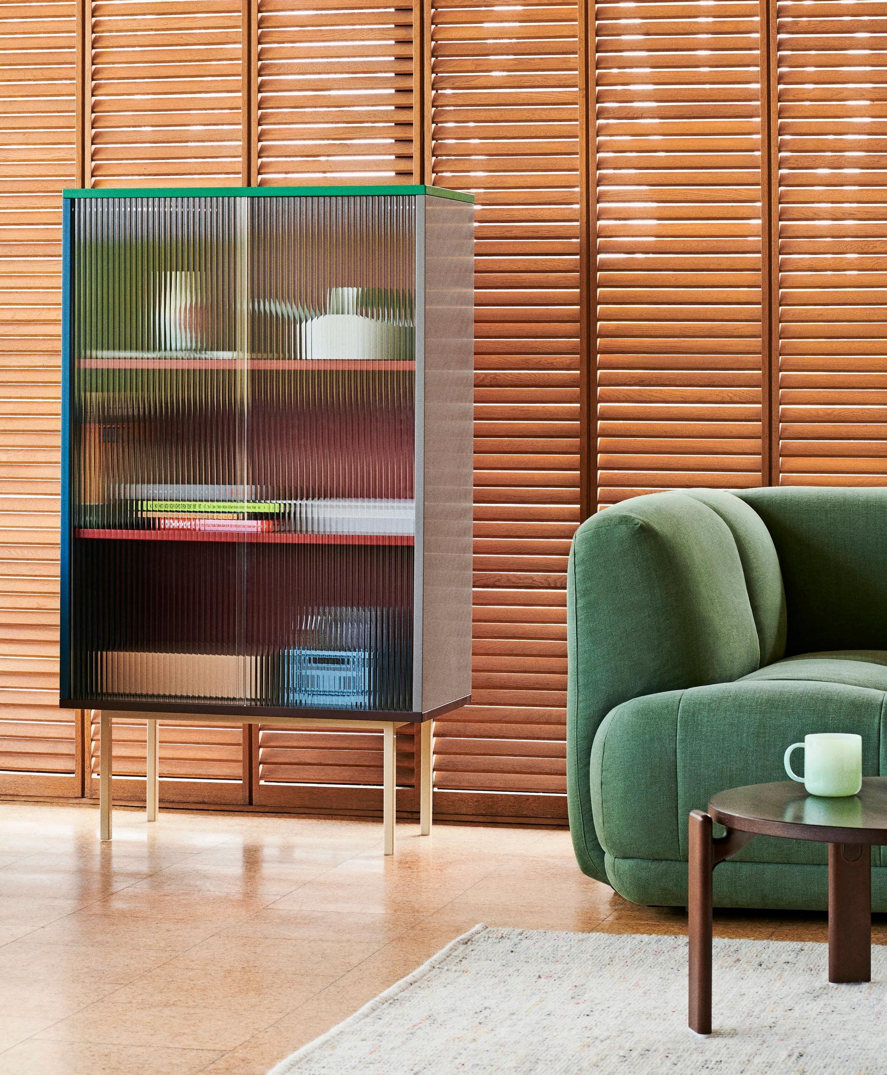 Hayn Colour Cabinet -kaappi, jossa raitalasiovet ja esineitä, vihreä sohva ja tumma sohvapöytä, taustalla puusälekaihtimet