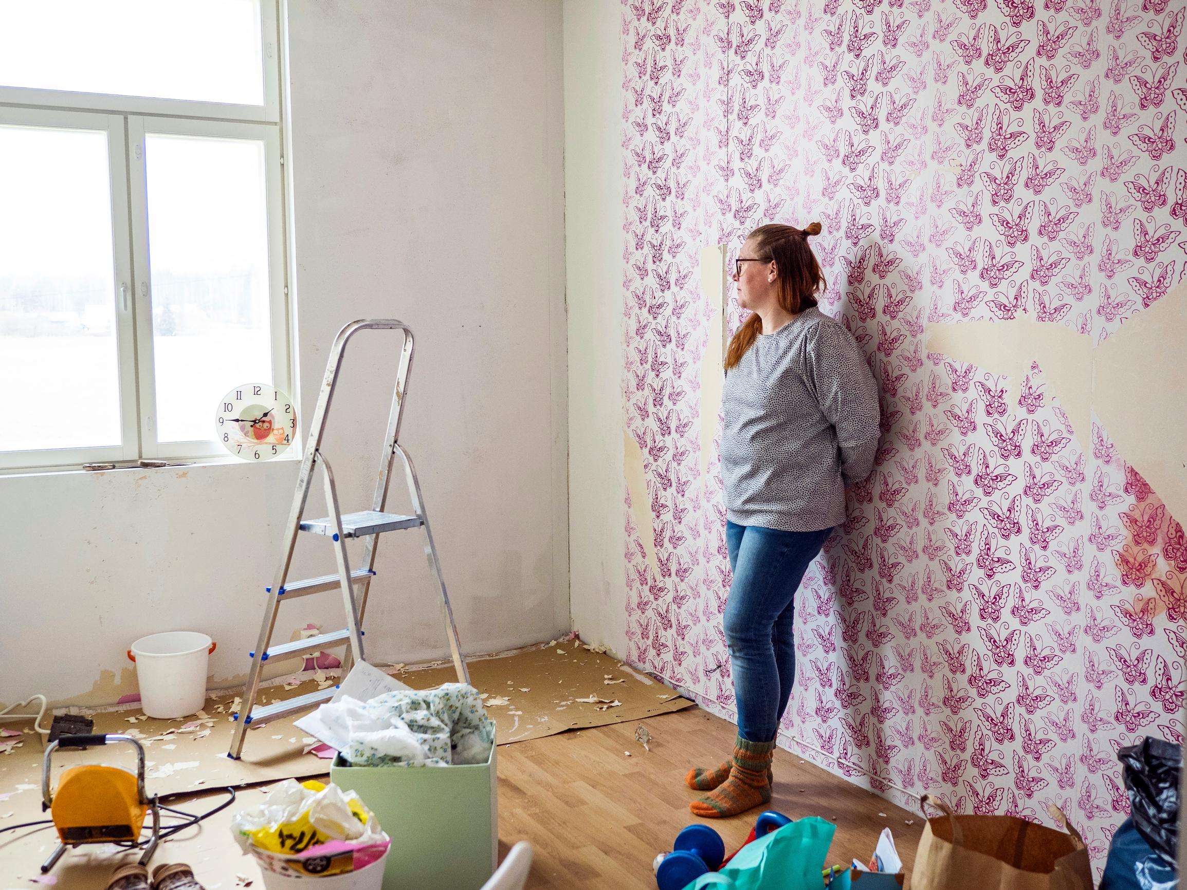 nainen nojaa seinään, jonka tapetti on repeillyt