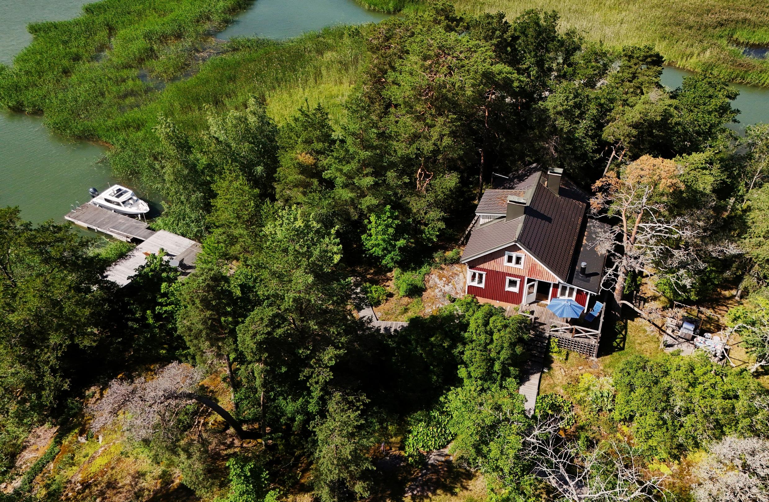 Helin saarimökki ilmakuvassa, kallioita ja metsää, venelaituri ja merta