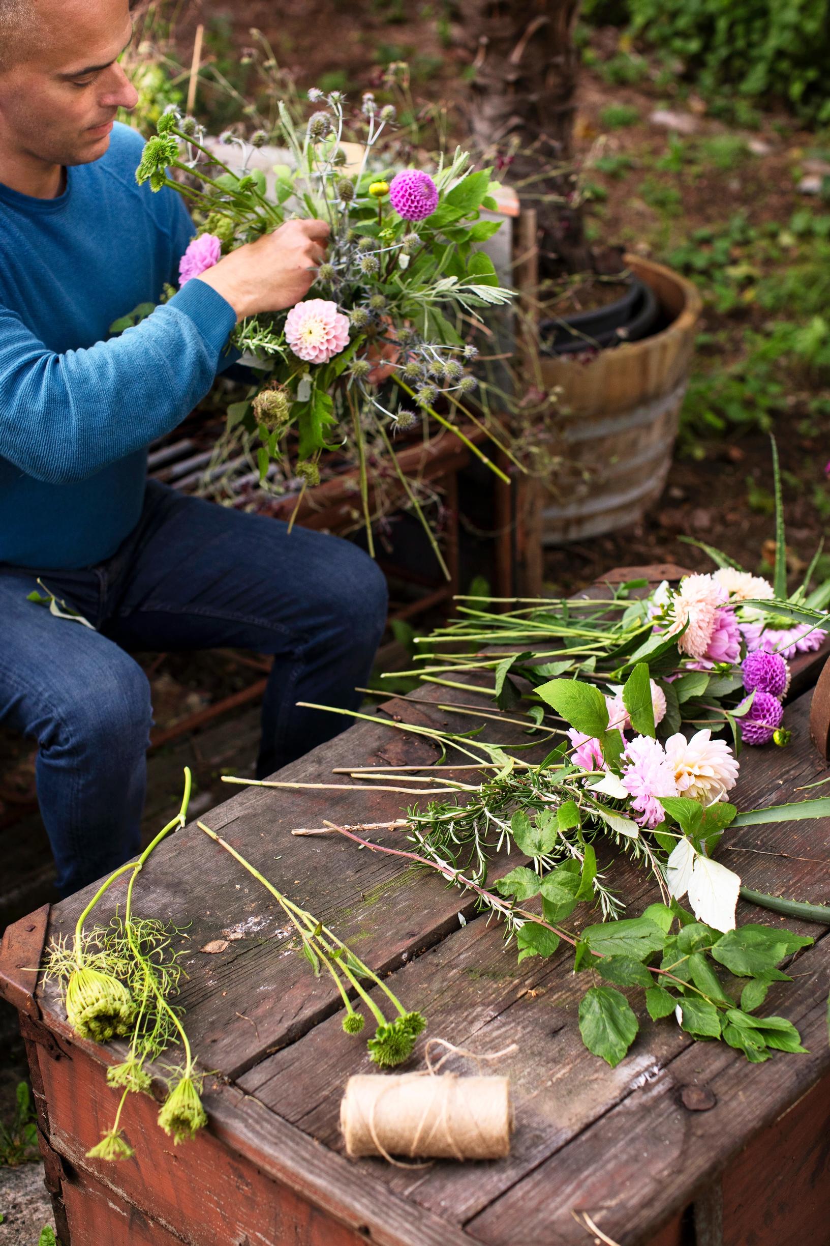 Tommi kokoamassa kukkakimppua violeteista ja vaaleanpunaisista kukista