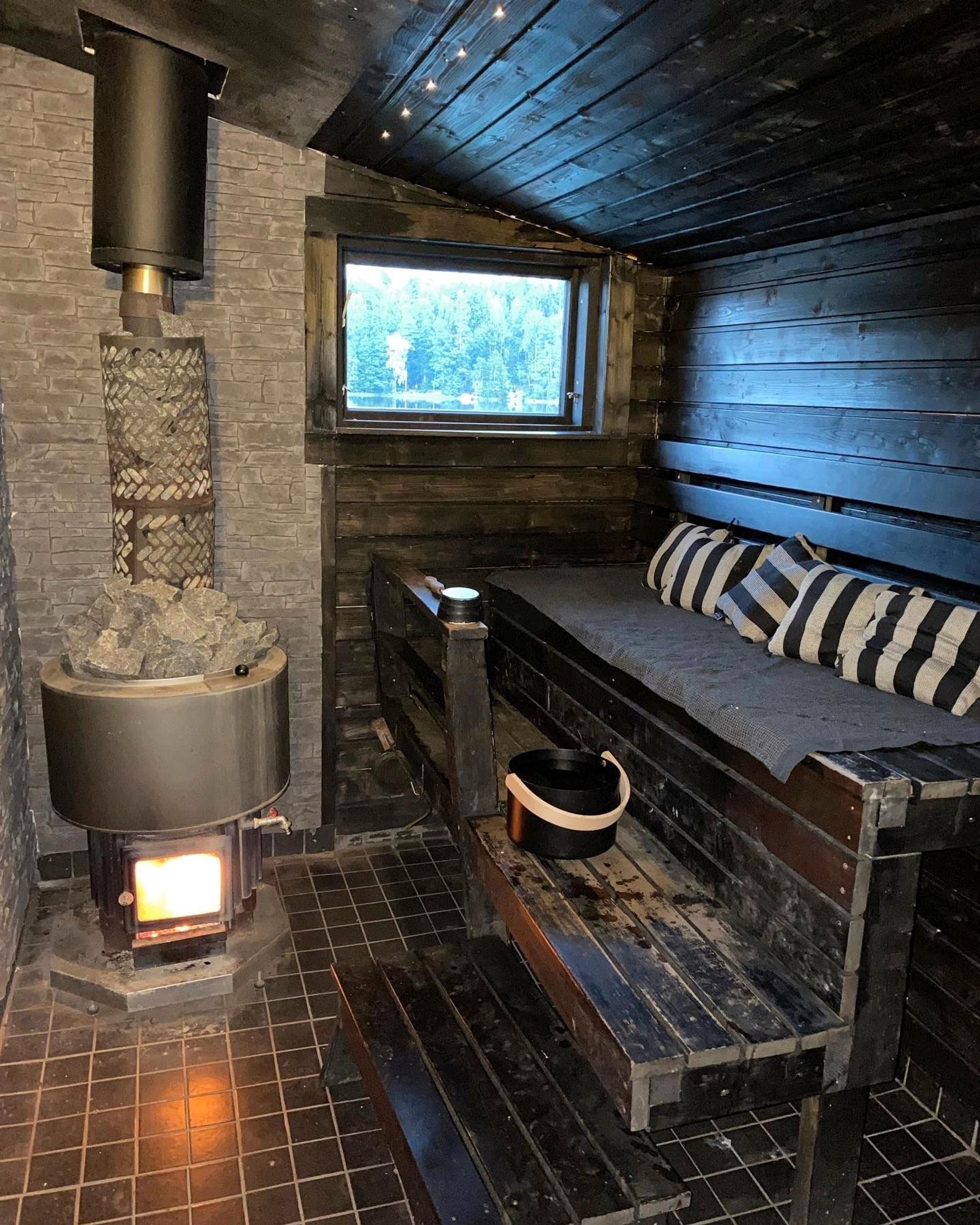 Supernanny Pia Penttalan tummasävyinen sauna, kiukaassa tuli, raidalliset saunatyynyt