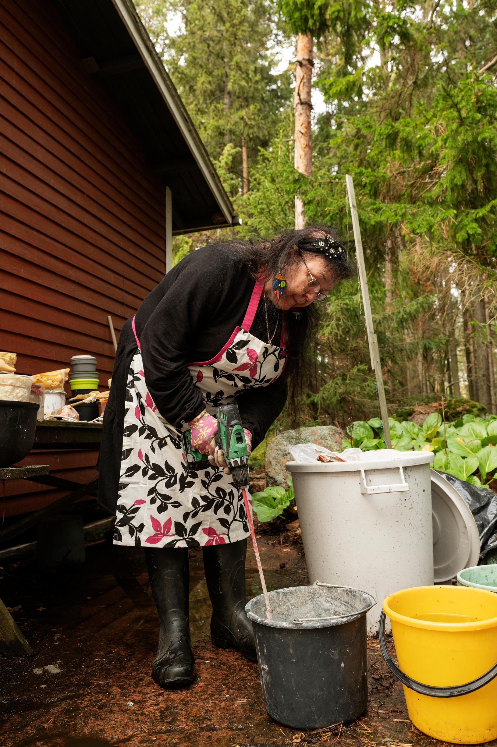 Arja Ögård sekoittaa sähkötyökalulla betonia ämpärissä mökin pihalla