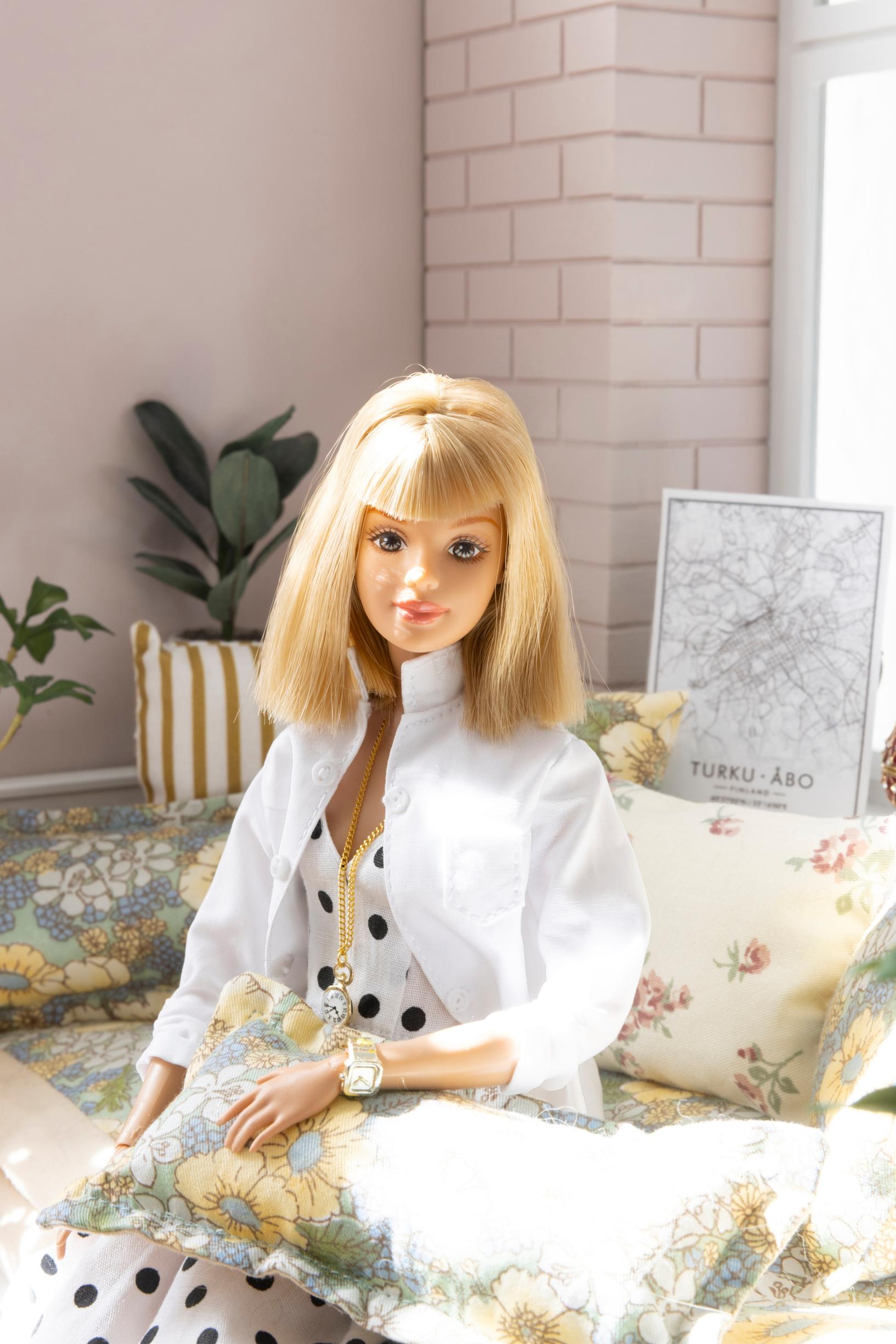 Barbie-nukke istuu sohvalla sohvatyyny sylissään