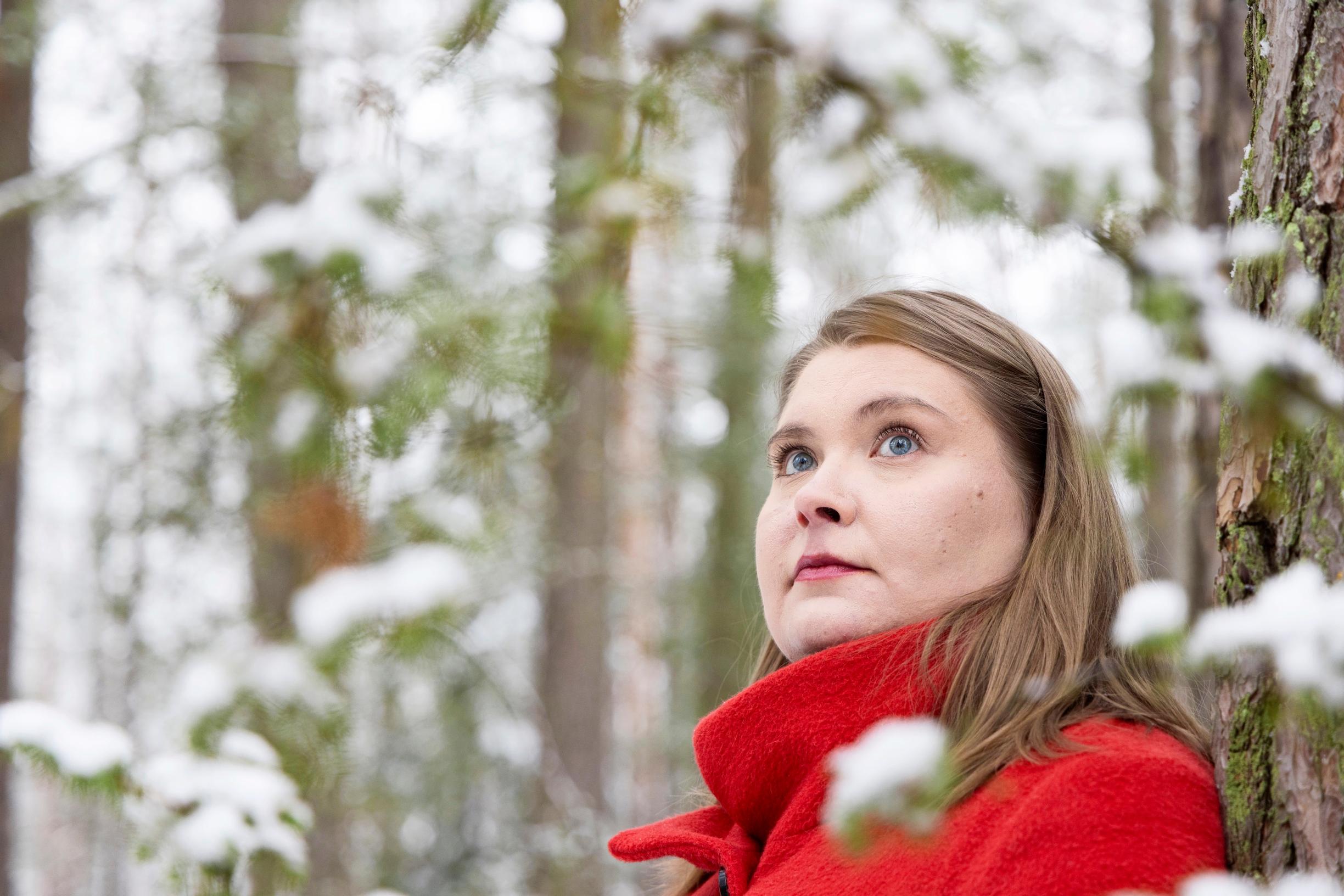 nainen nojaa männyn runkoon metsässä
