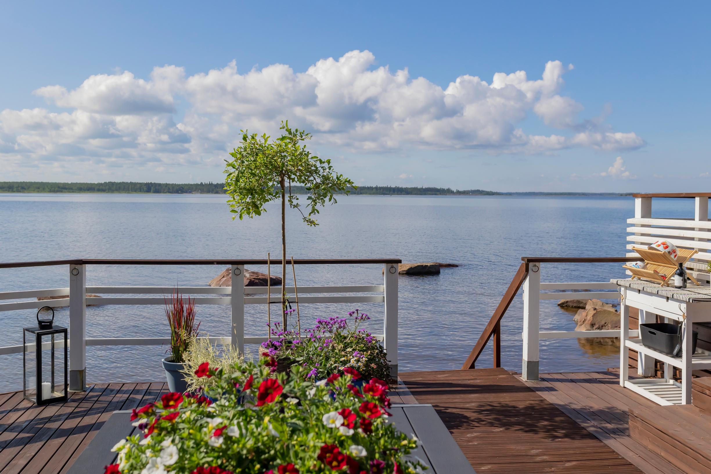 terassilla kesäkukkia, lyhty ja sivupöytä, portaat alas ja meri