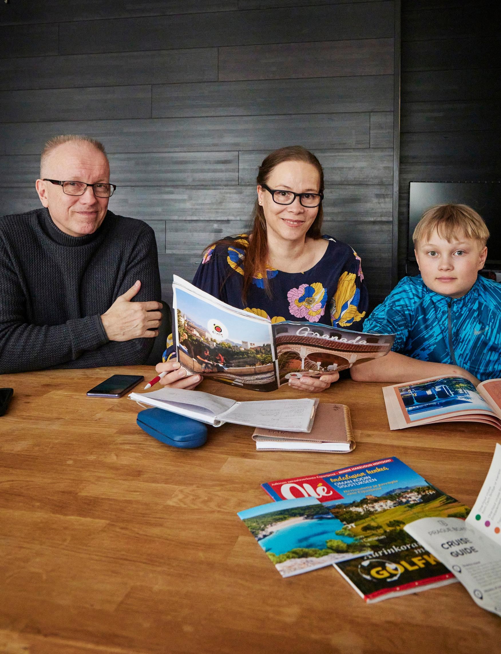 perhe istuu pöydän ääressä, pöydällä on esillä matkailuesitteitä ja muistiinpanoja