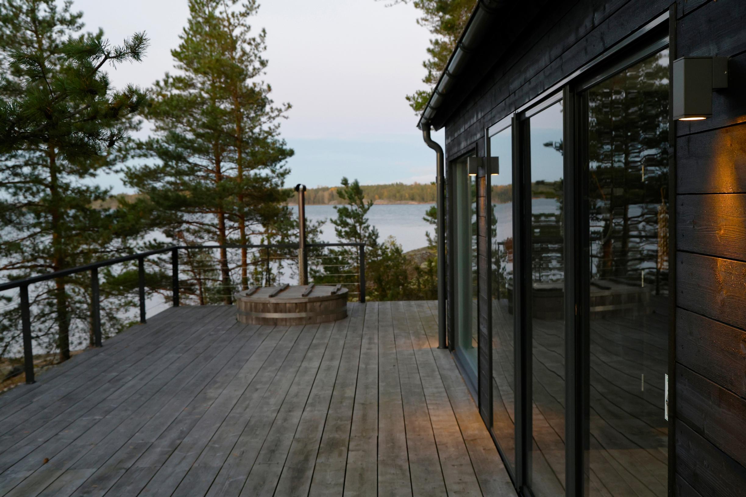 mustan mökin lasi-ikkunat, terassi, palju ja merimaisema