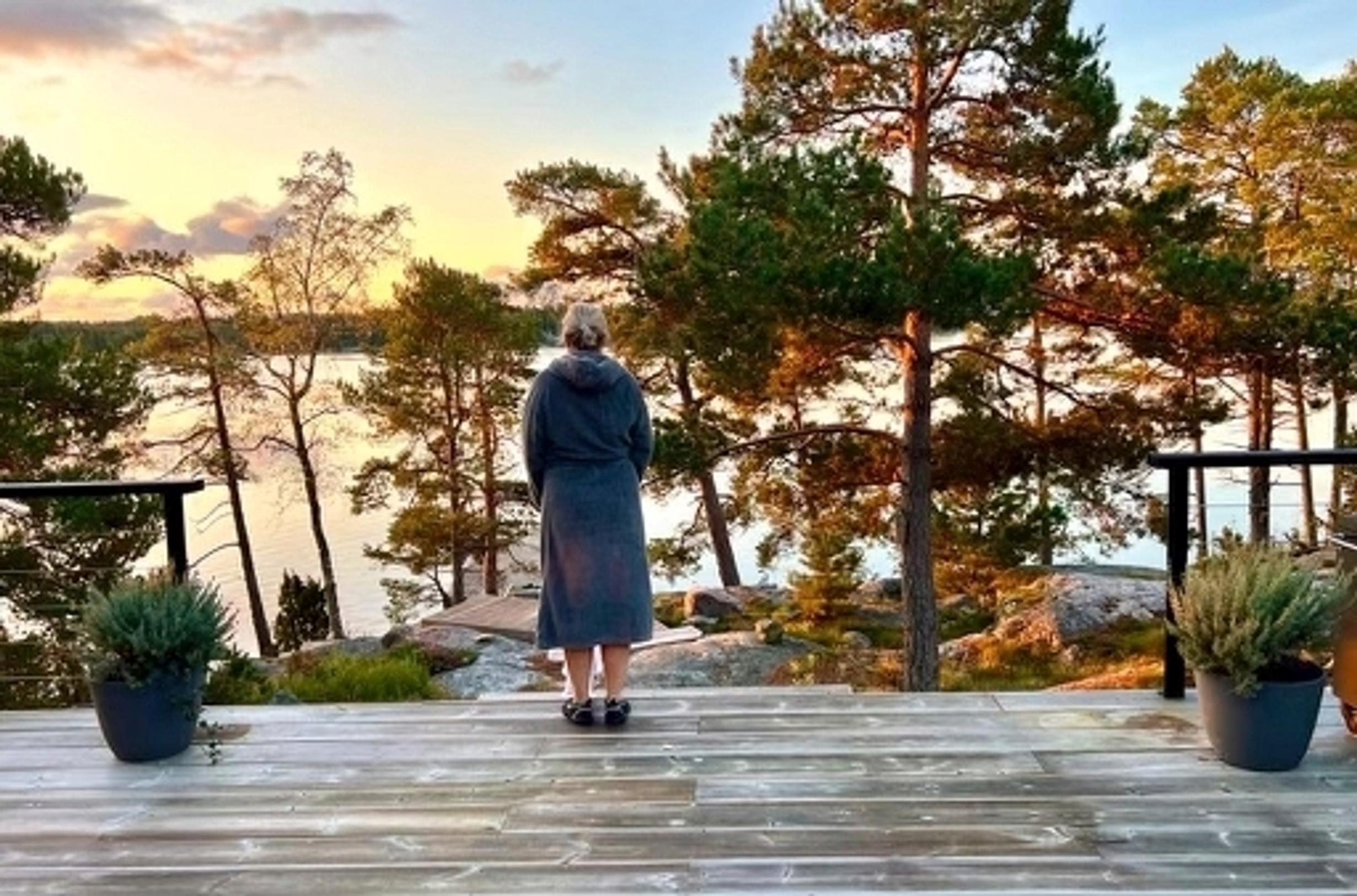 Jani Vahvanen selin katselemassa kylpytakissa terassilta merelle auringonlaskussa