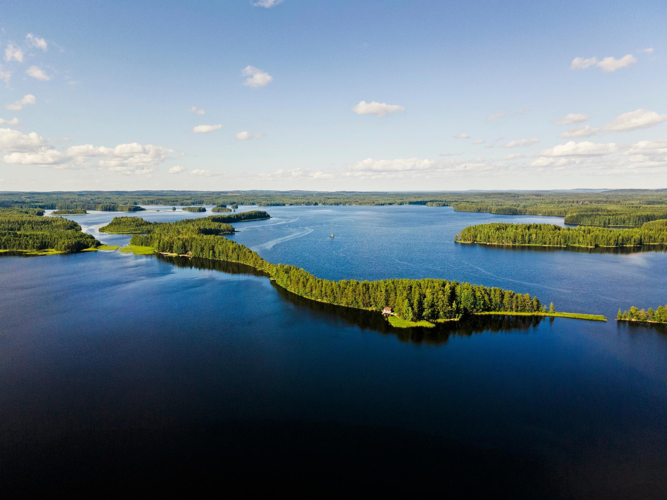 ilmakuva Saimaalta, järveä, saaria ja metsää, taivaalla valkoisia pilviä