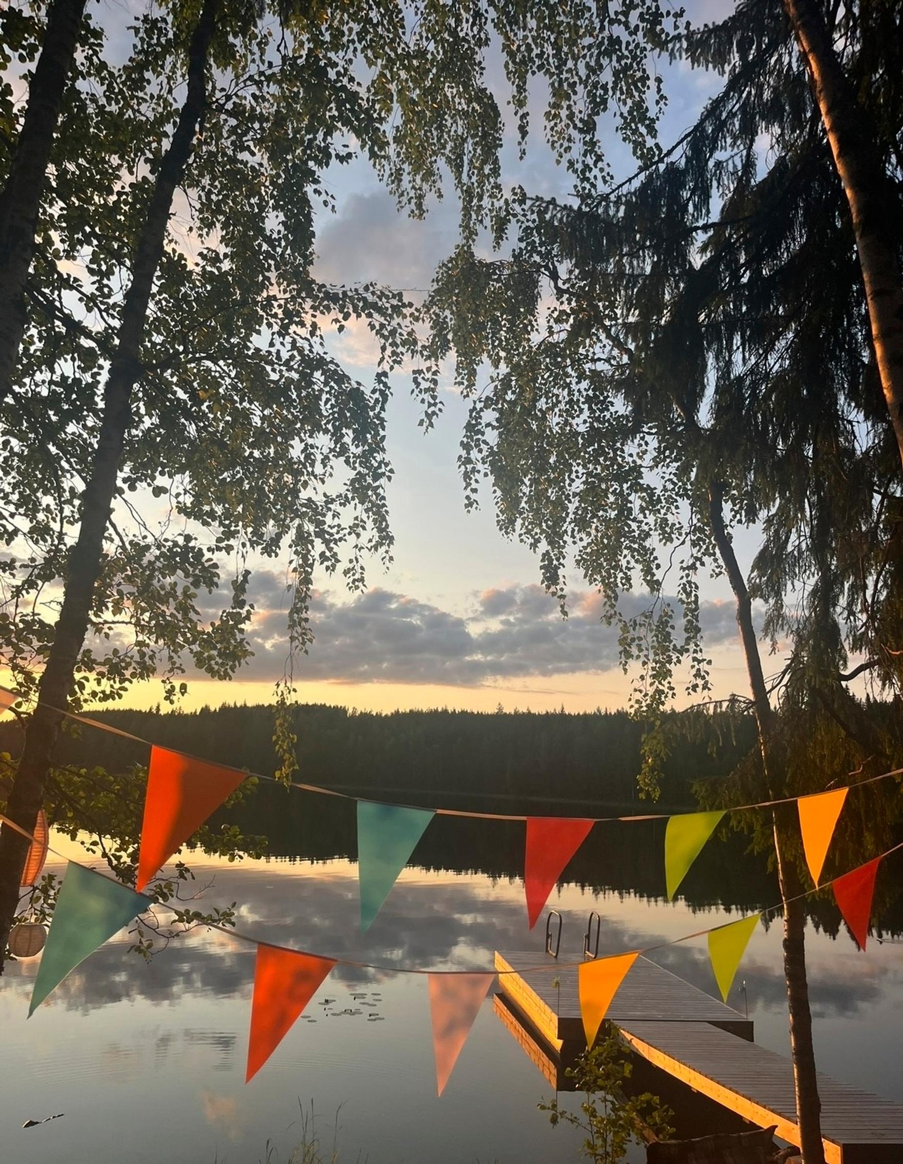 Värikäs viirinauha ripustettuna järven rantaan, ilta-aurinko osuu laiturille