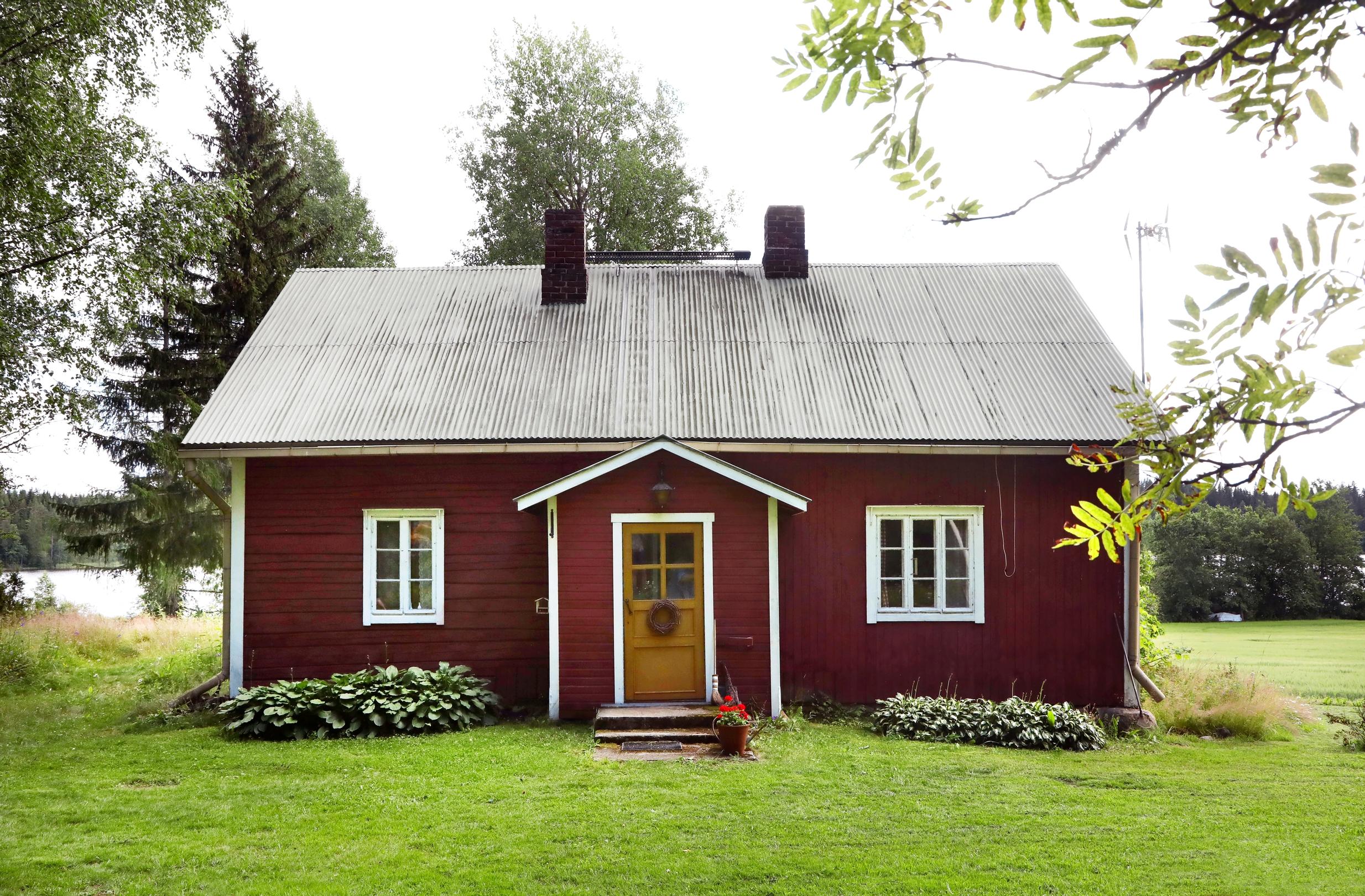 Punamullattu talo nurmikentä keskellä, taustalla näkyy järvi.