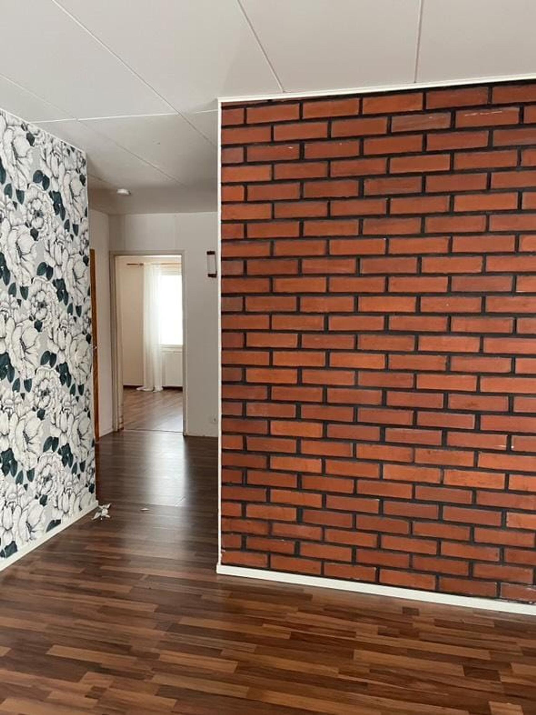 Huoneessa on tumma parketti, tiiliseinä ja kuviotapetilla tapetoitu tehosteseinä